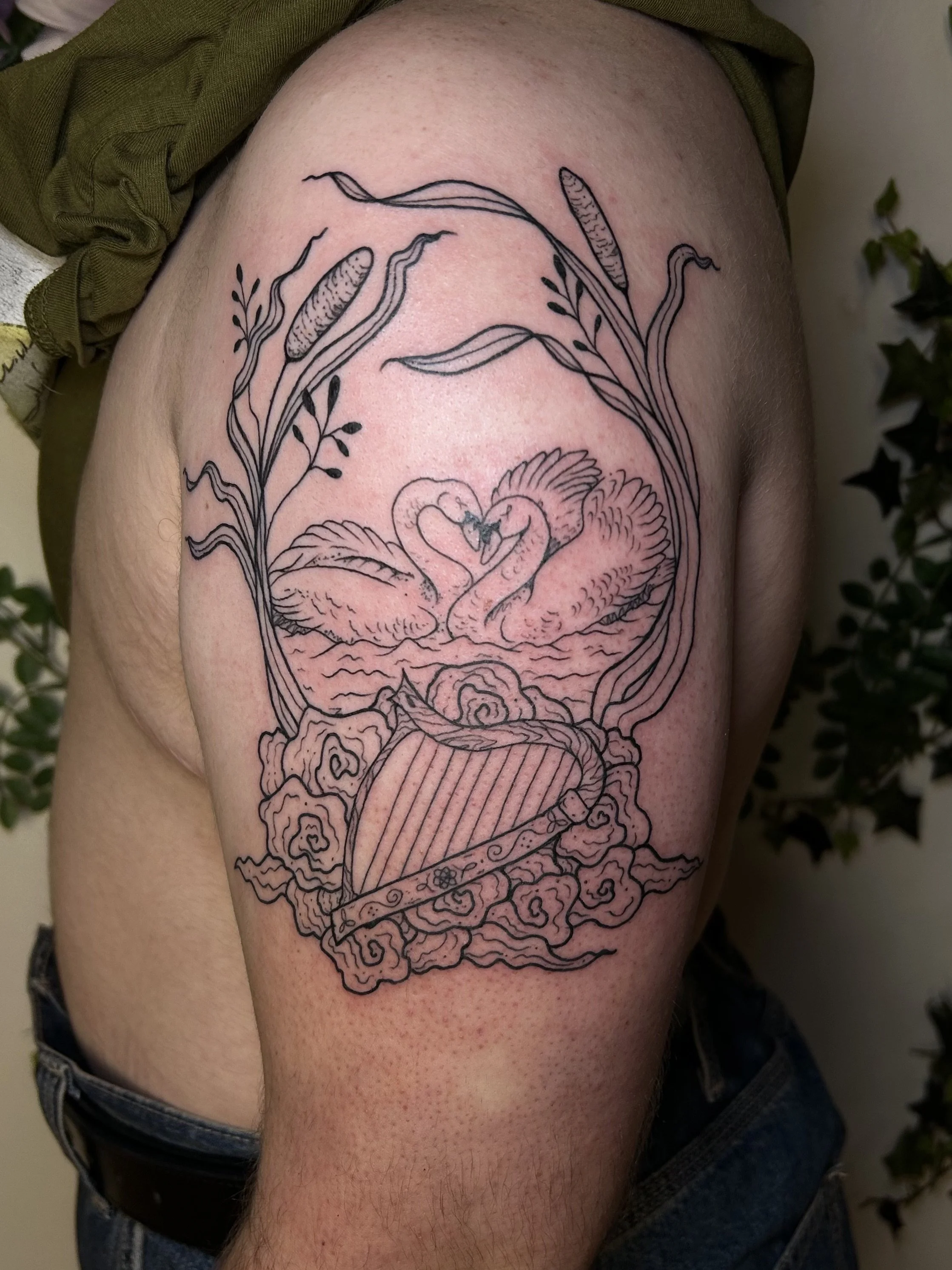 Linework swans, harp, and cattails scene on upper arm
