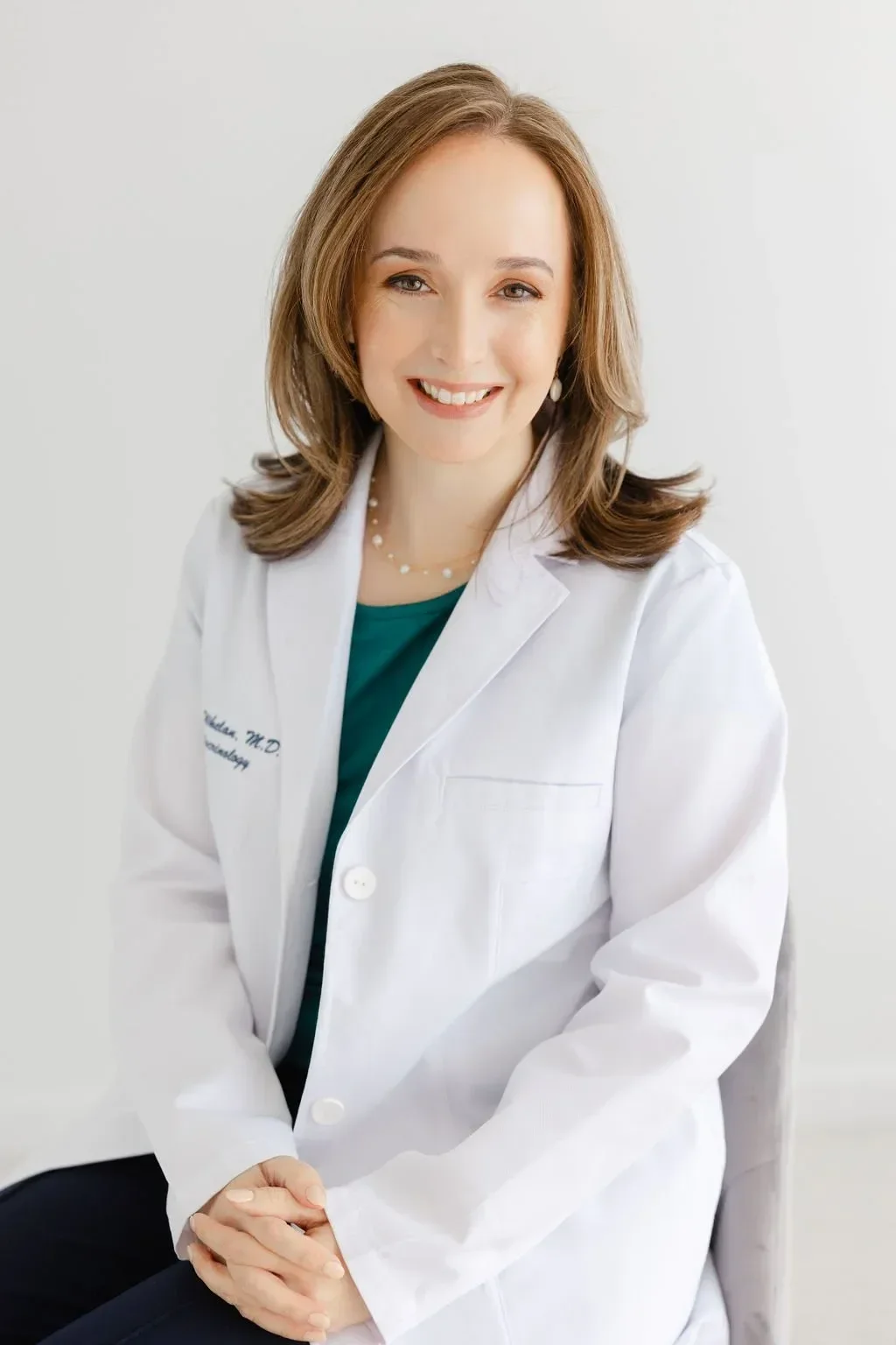 Dr. Whelan in a white lab coat sits against a light background. She has shoulder-length hair and wears a green top, conveying a professional yet warm demeanor.
