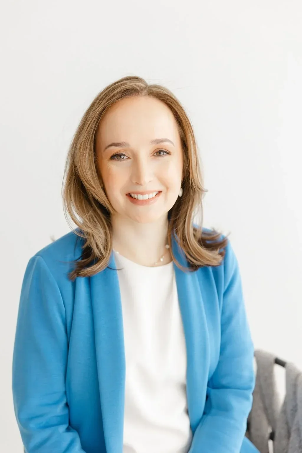 Dr/ Whelan in a blue blazer and white blouse against a plain white background. She has shoulder-length brown hair, conveying a professional and approachable demeanor.