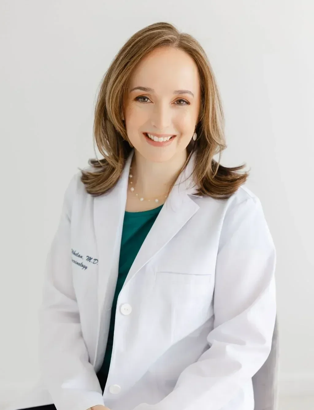 Portrait of Dr. Mae Whelan wearing a white medical coat and a green top, with a light background.
