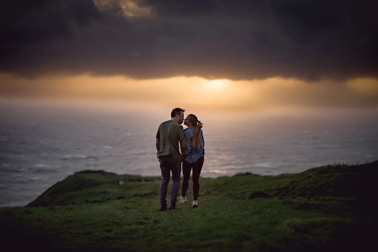 Romantic couple walking together at sunset during a Cliffs of Moher proposal photography session overlooking the Atlantic Ocean.