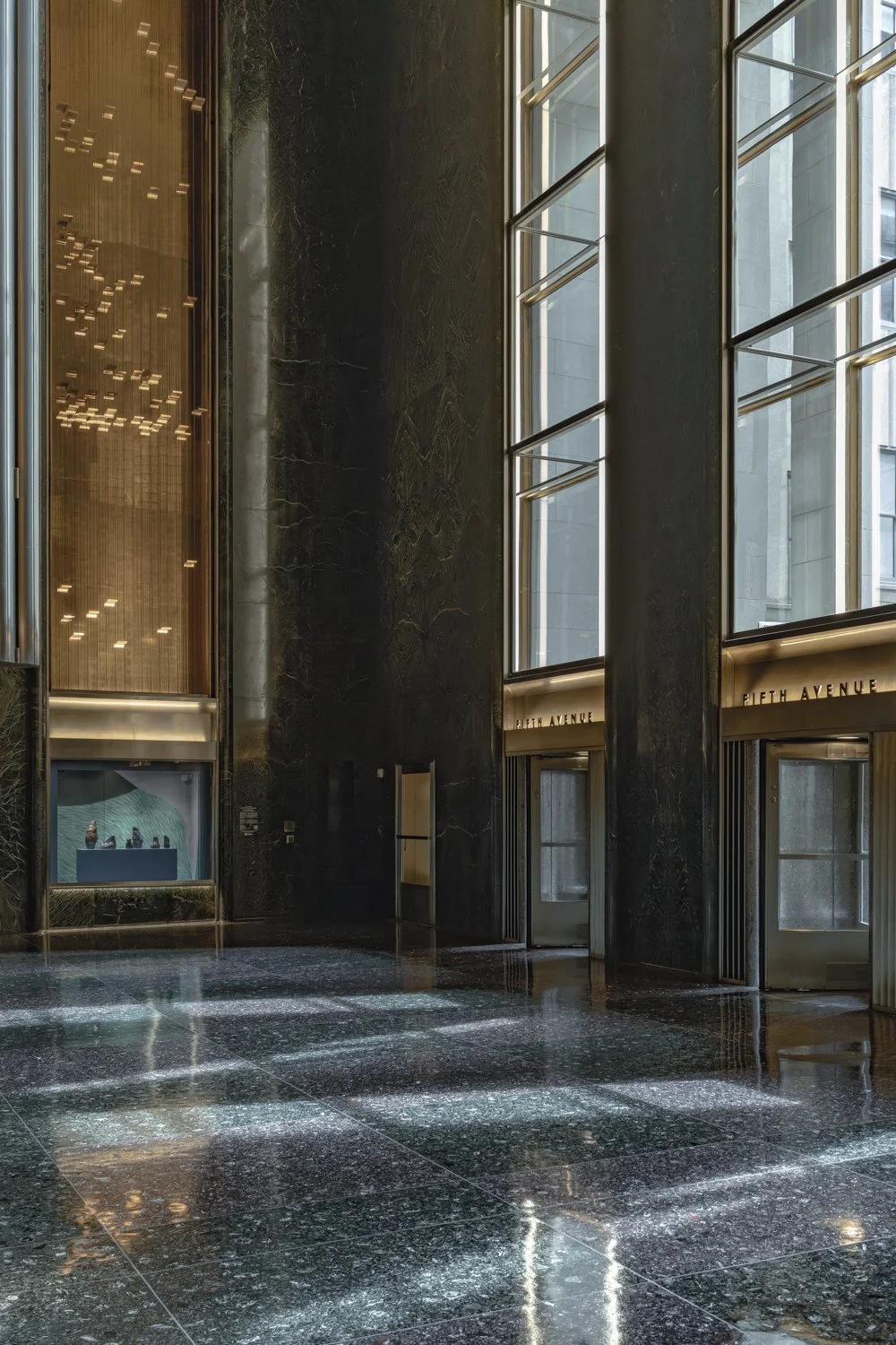 Interior of a modern building lobby with large black marble walls, tall glass windows, and a polished marble floor reflecting the surroundings.