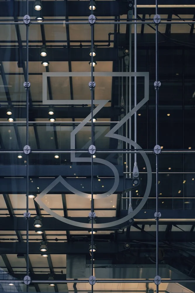 Modern glass building with a large London Underground logo, reflecting interior lights and structural details.