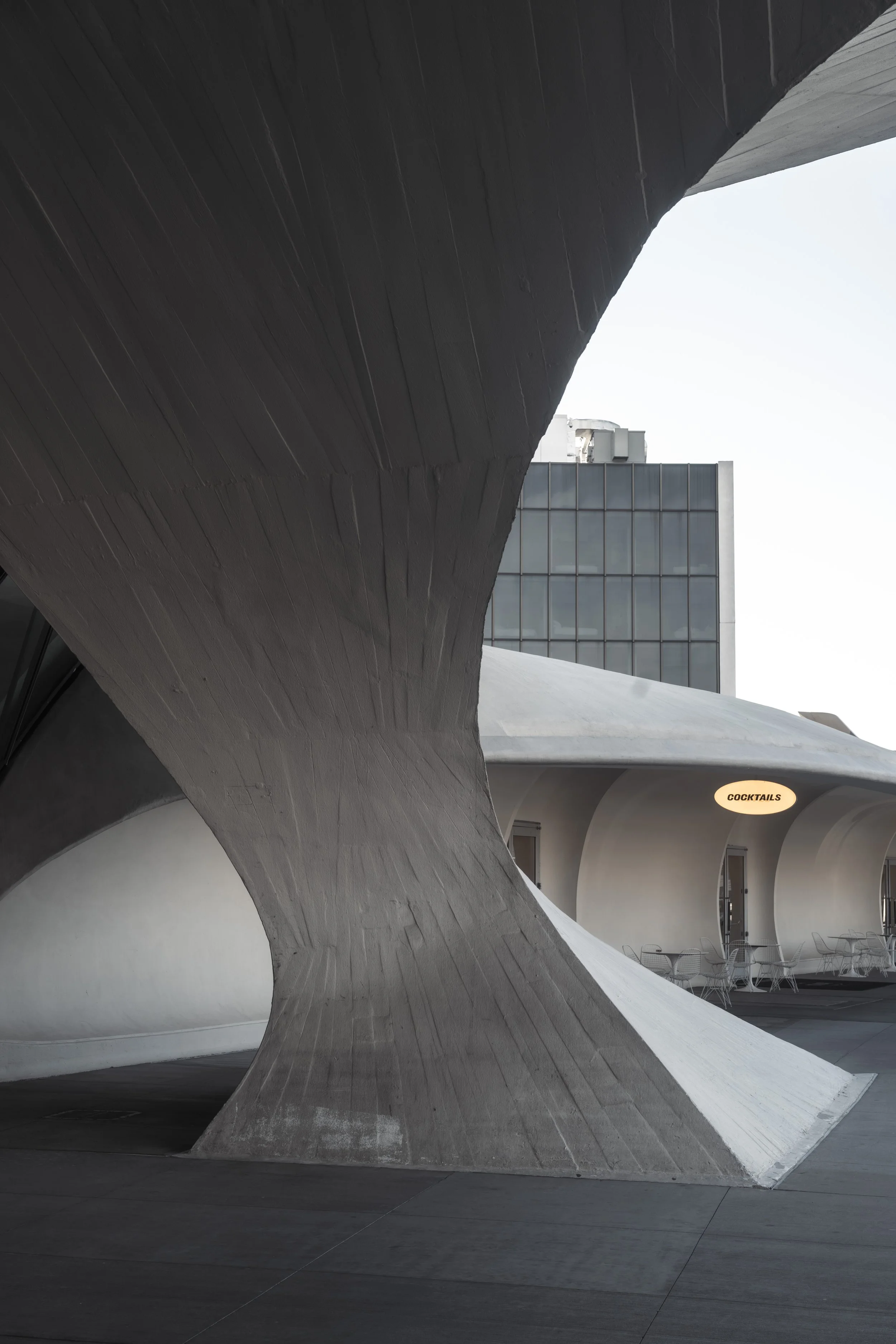 Modern architectural building with curved concrete structure and a sign that reads 'Cocktails' near outdoor seating.