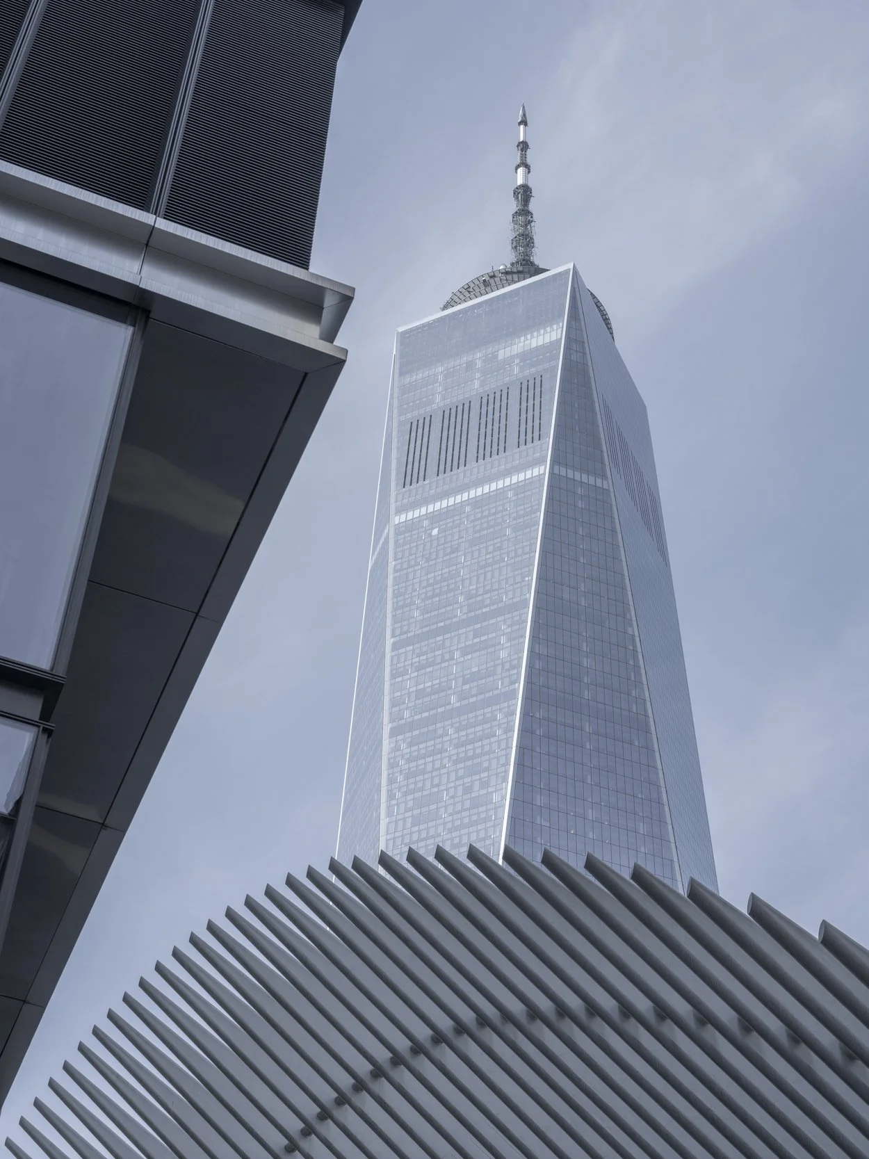 View of One World Trade Center in New York City from below, with modern building architecture in the foreground.
