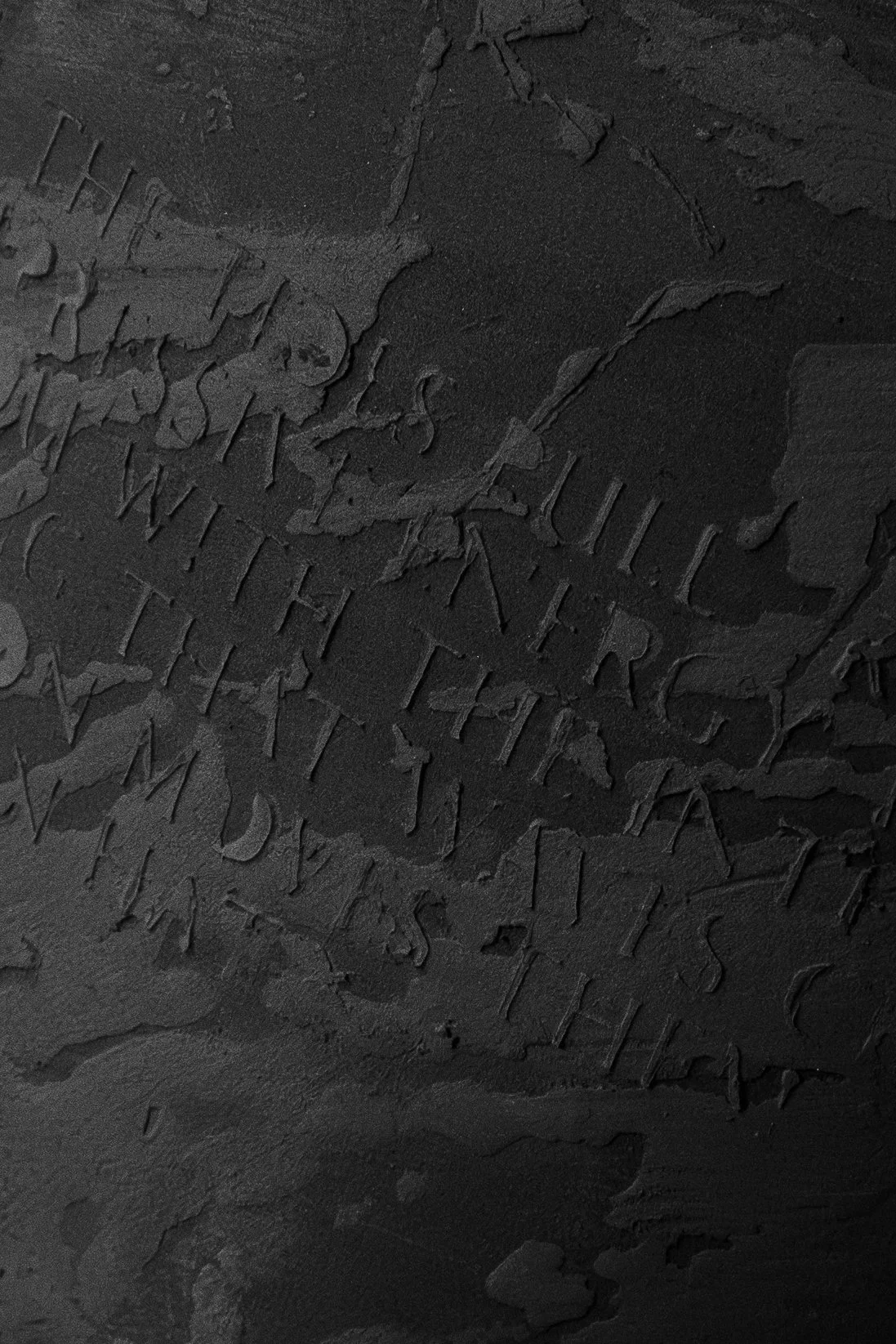 Close-up of a dark, textured surface with engraved or embossed text, partially obscured and difficult to read.