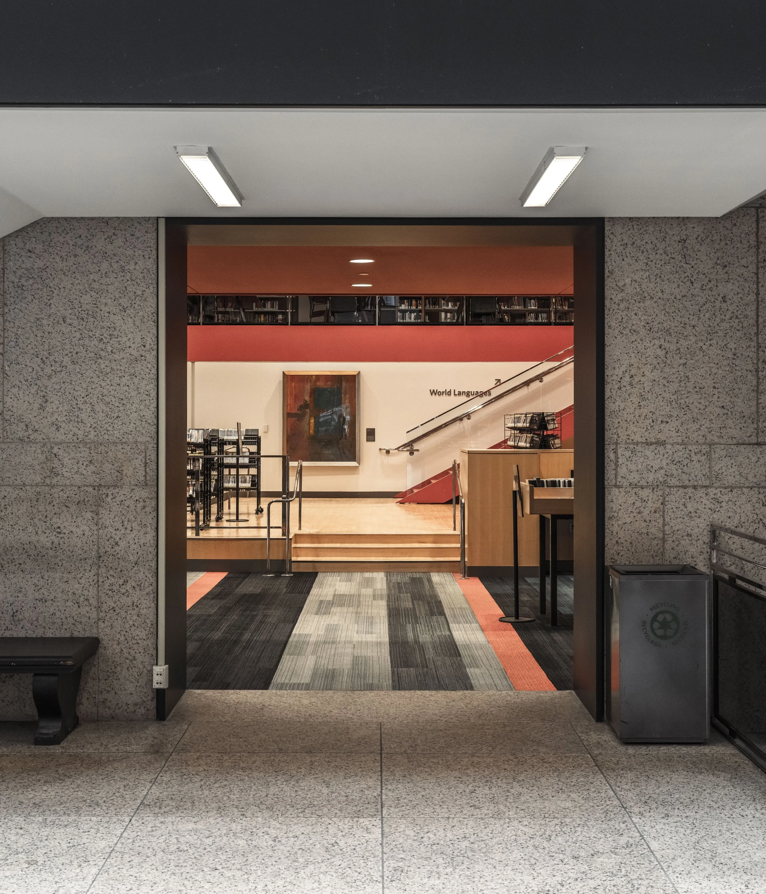 Entrance to a library with a view of bookshelves and a staircase leading to a second level marked 'World Languages'.
