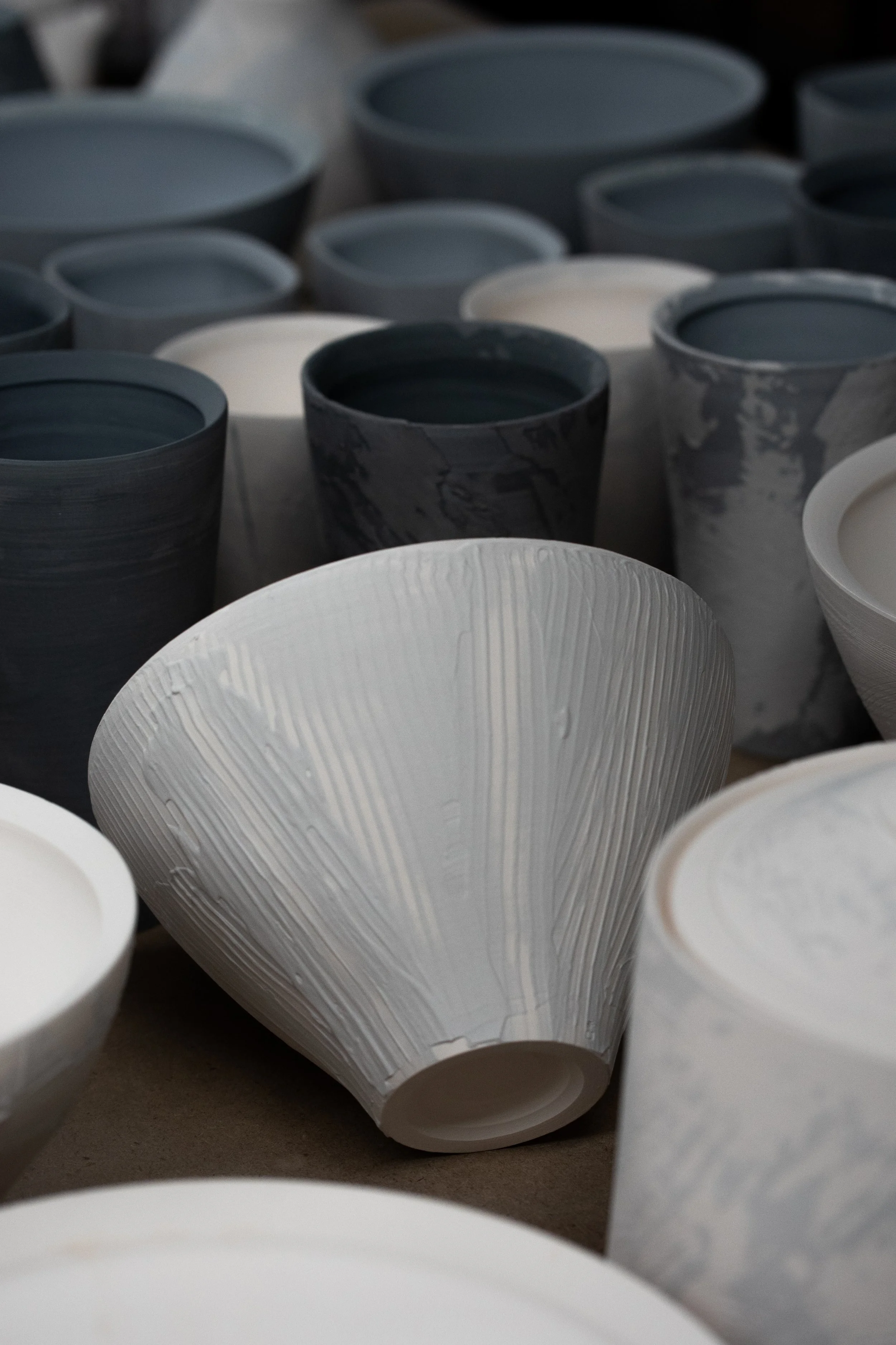 Various ceramic bowls and vases in neutral tones, including white, gray, and black marbled patterns, arranged on a surface and in a workshop setting.