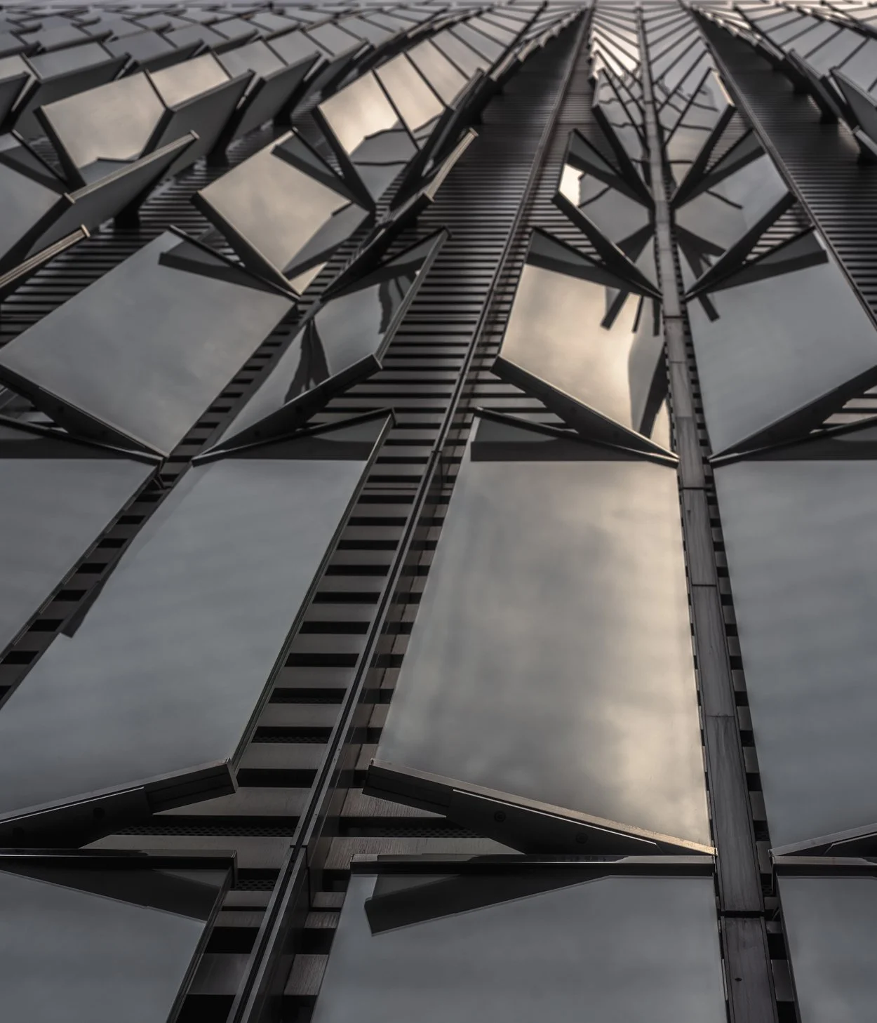 Looking up at the reflective glass windows and metal framework of a modern skyscraper.