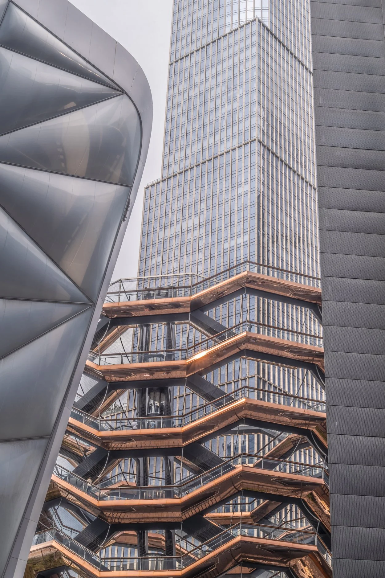 View of modern high-rise buildings with reflective glass windows, a distinctive external staircase with copper-colored railings, and metallic architectural elements.