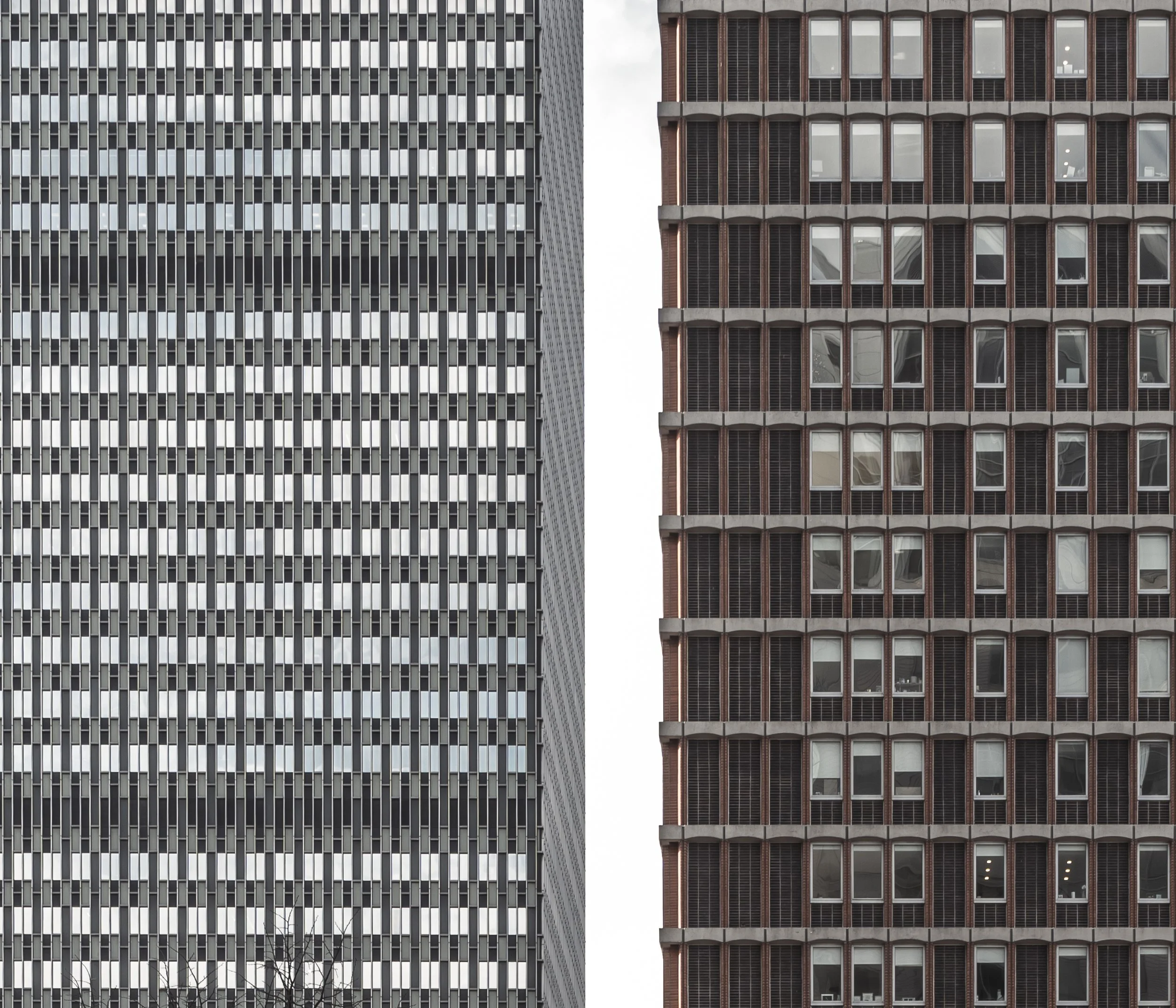 Two tall building facades side by side, one with a pattern of small black and white rectangular windows, the other with larger windows separated by horizontal and vertical concrete lines.