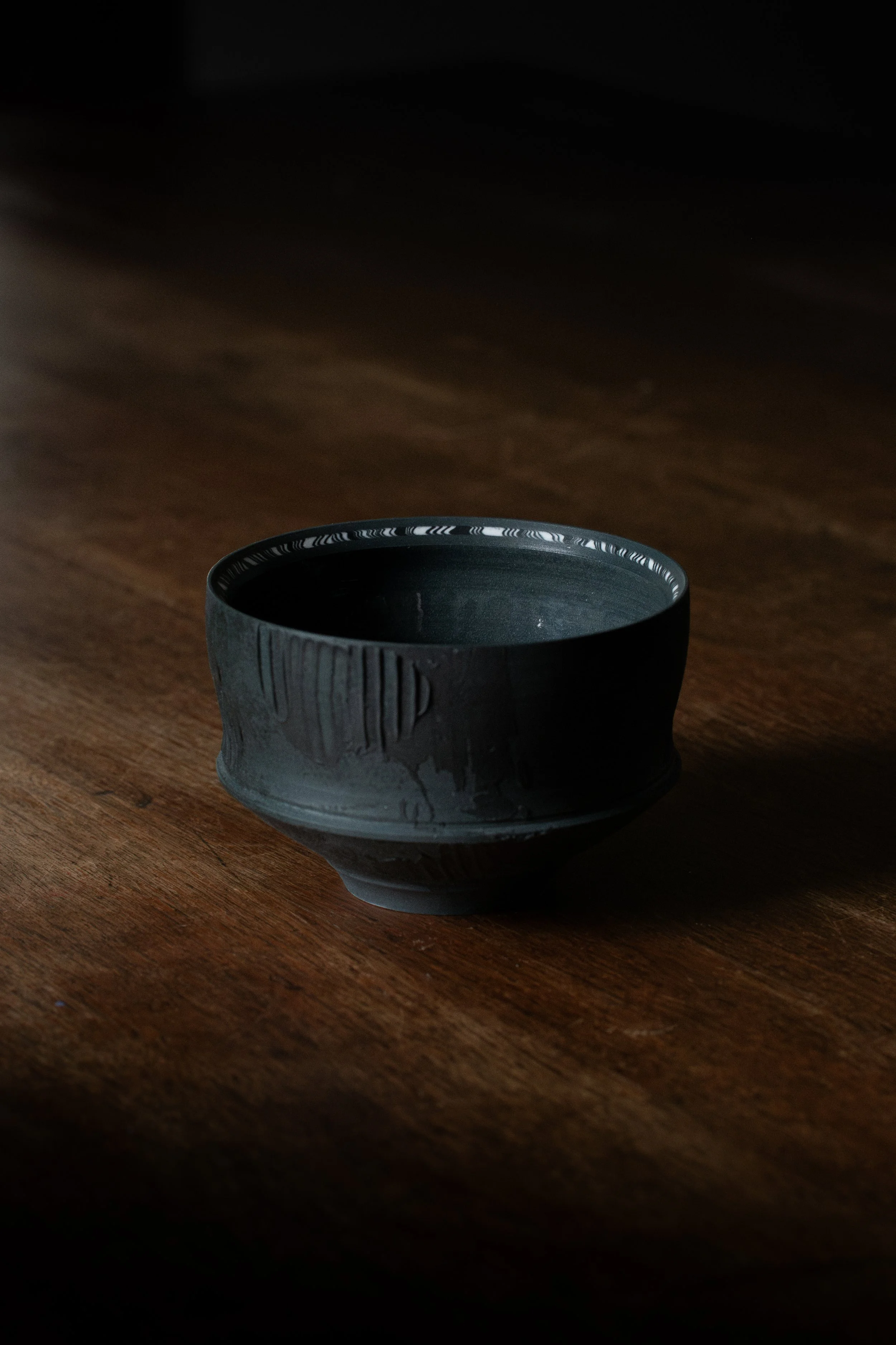 A black ceramic bowl placed on a wooden surface with a dark, shadowed background.