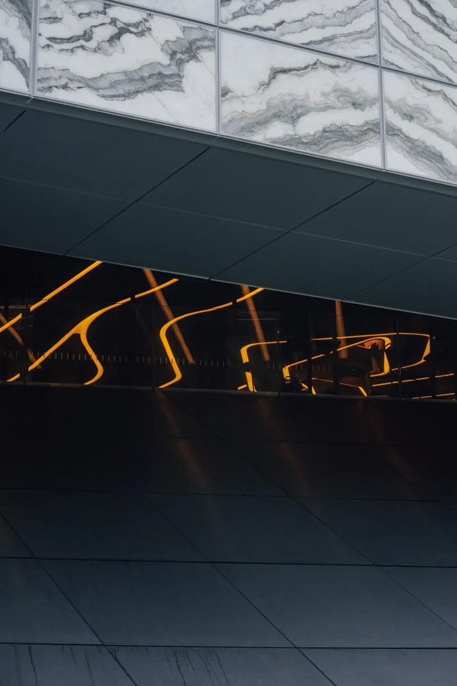 Modern architectural interior featuring marble walls, dark panels, and reflective glass with orange LED lighting patterns.