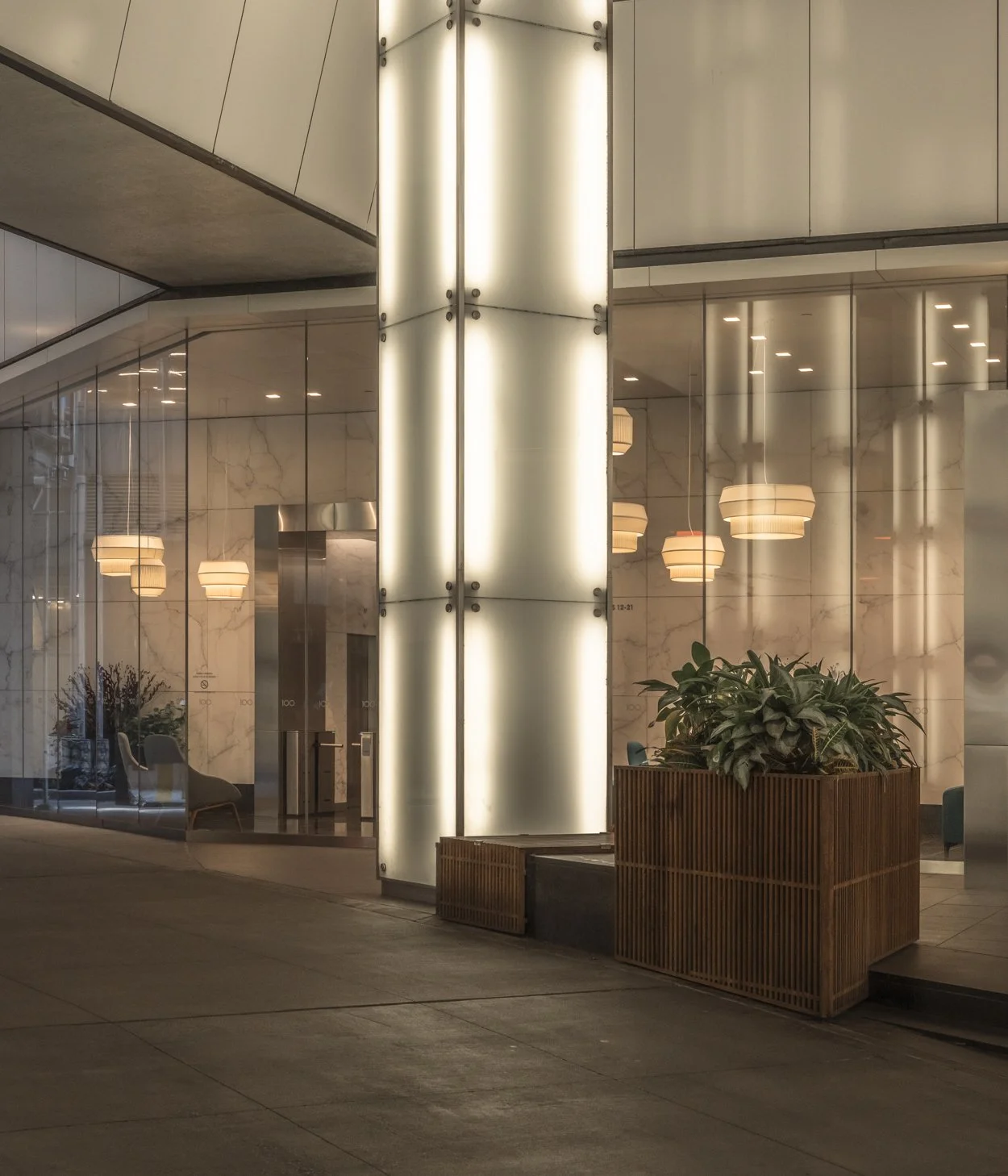 A modern building entrance with frosted glass panels, warm lighting fixtures inside, and a large potted plant outside.