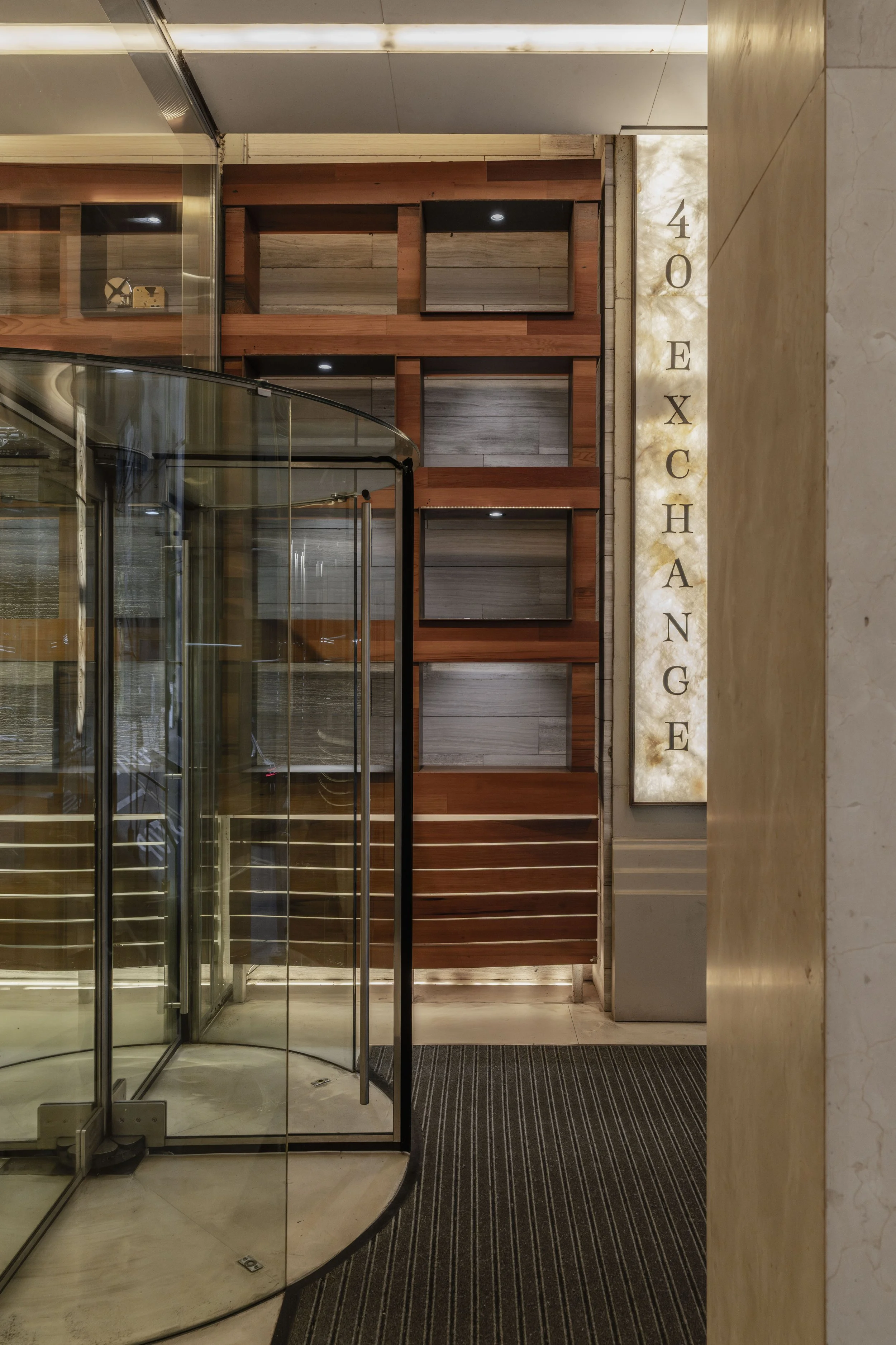 Interior view of a hotel lobby with a glass revolving door, wood paneling on the wall, and a backlit vertical sign reading '40 EXCHANGE'.