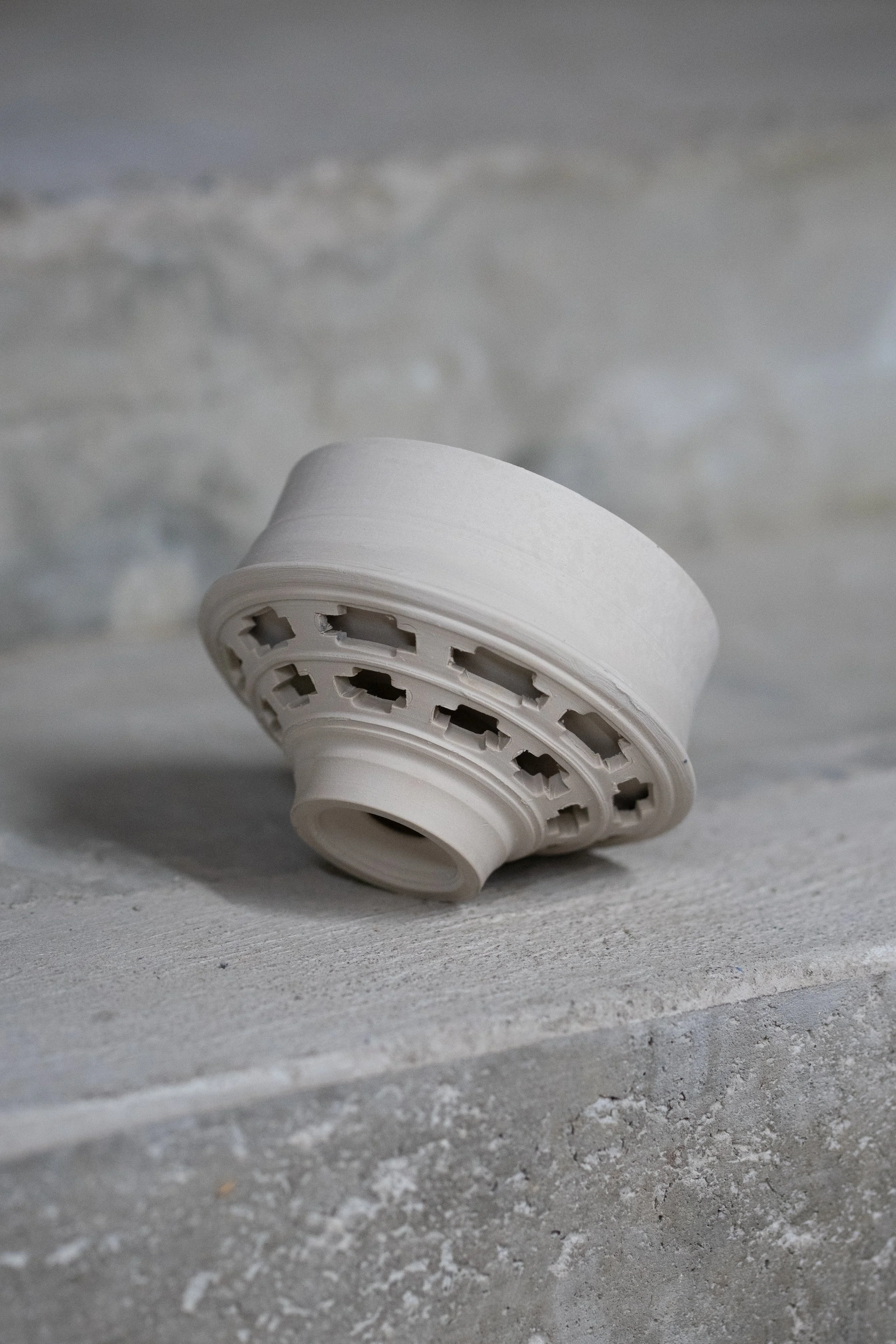 A smoke detector lying on a concrete surface against a concrete wall background.