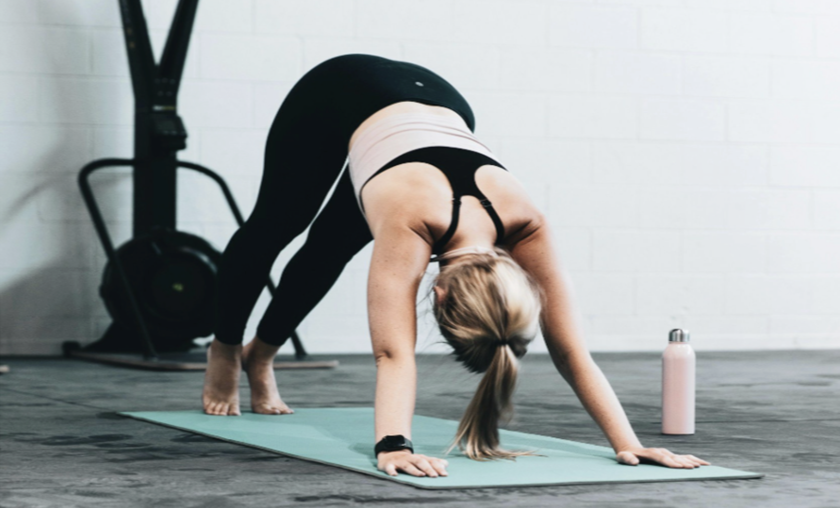 Person practicing yoga in downward dog pose on a turquoise mat with a water bottle nearby.