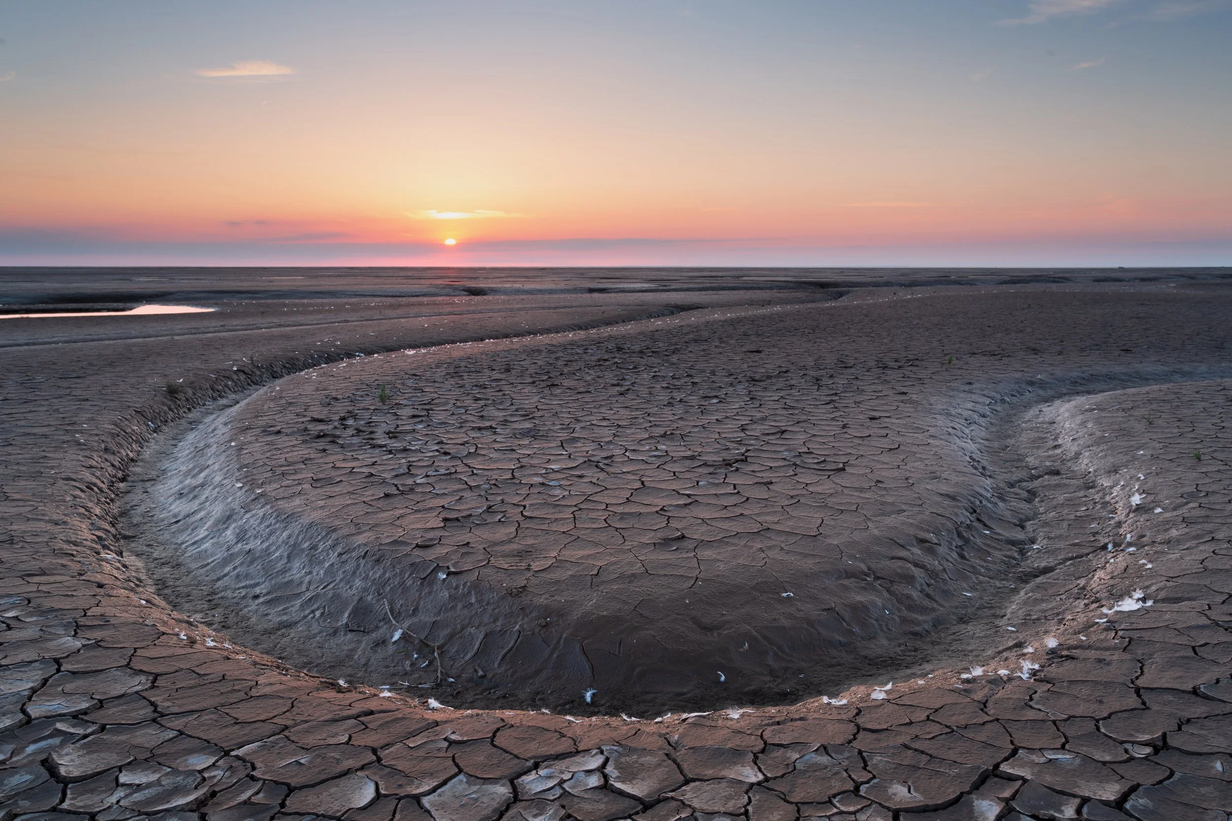 Dry cracked earth with water flowing into a circular depression at sunset.