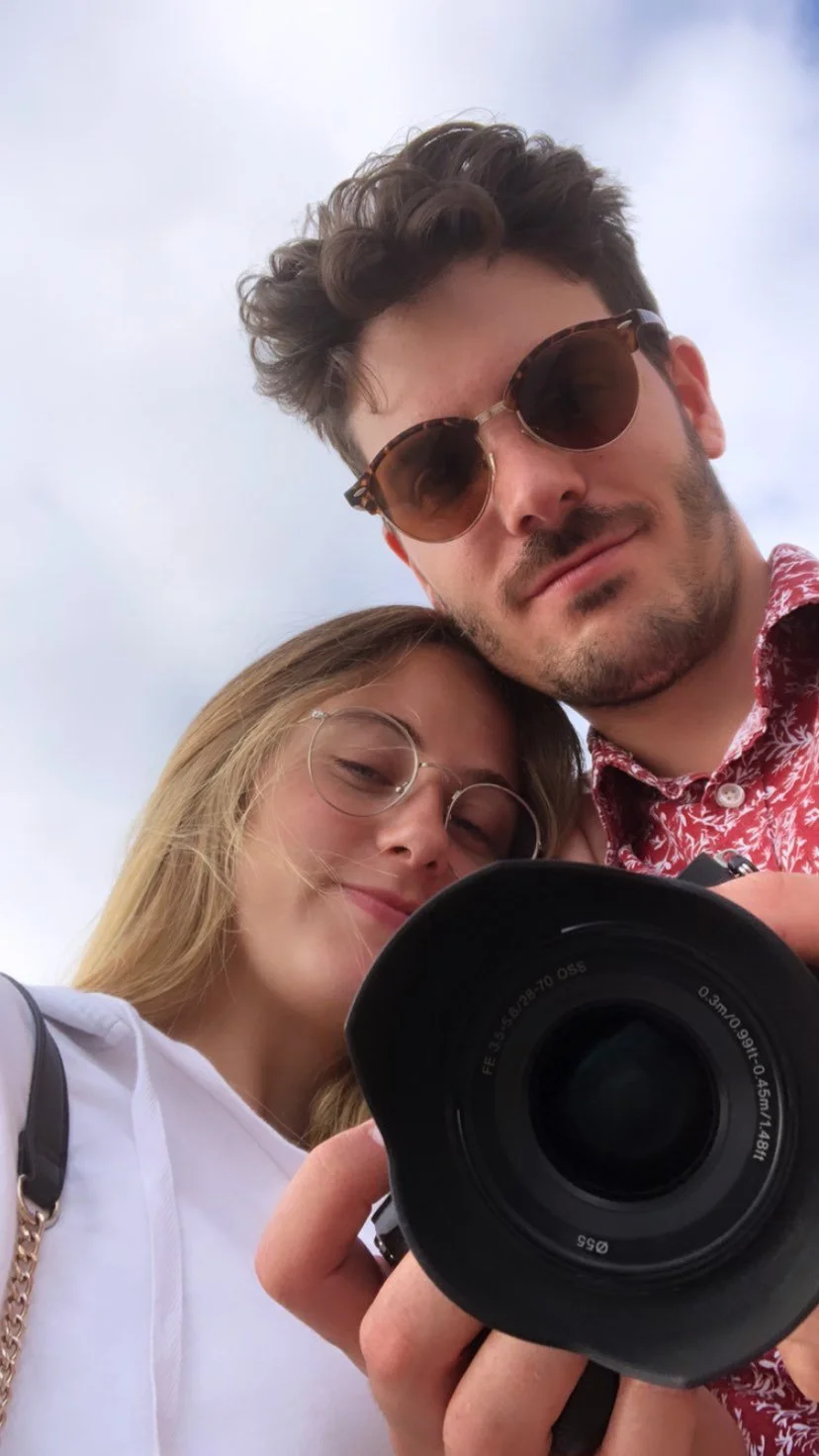 Una pareja joven toma una selfie con una cámara profesional bajo un cielo nublado.