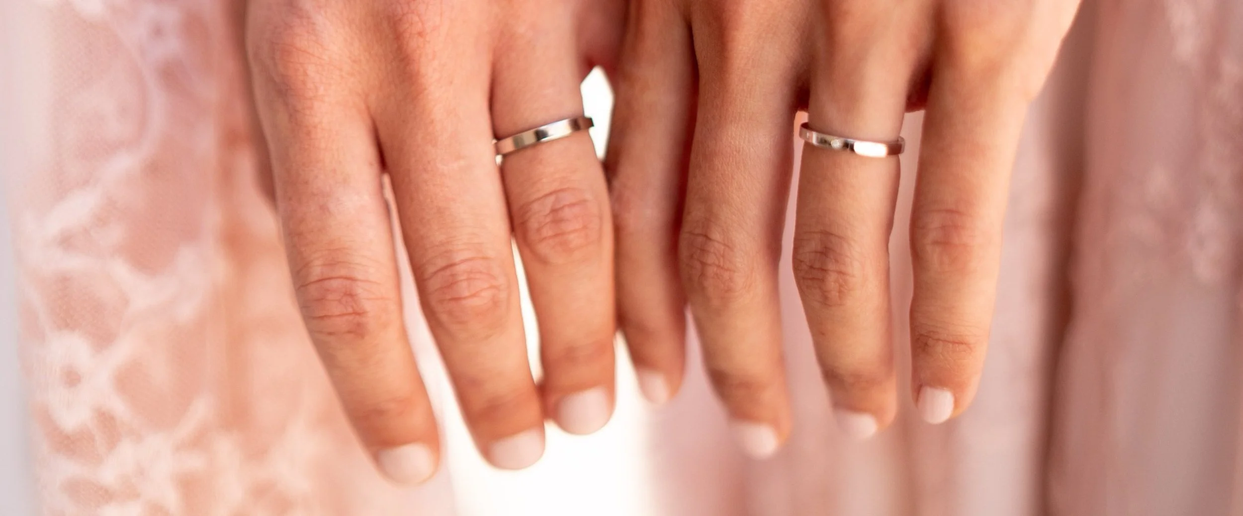 Manos de mujer con anillos de plata, sobre tela rosada con encaje.