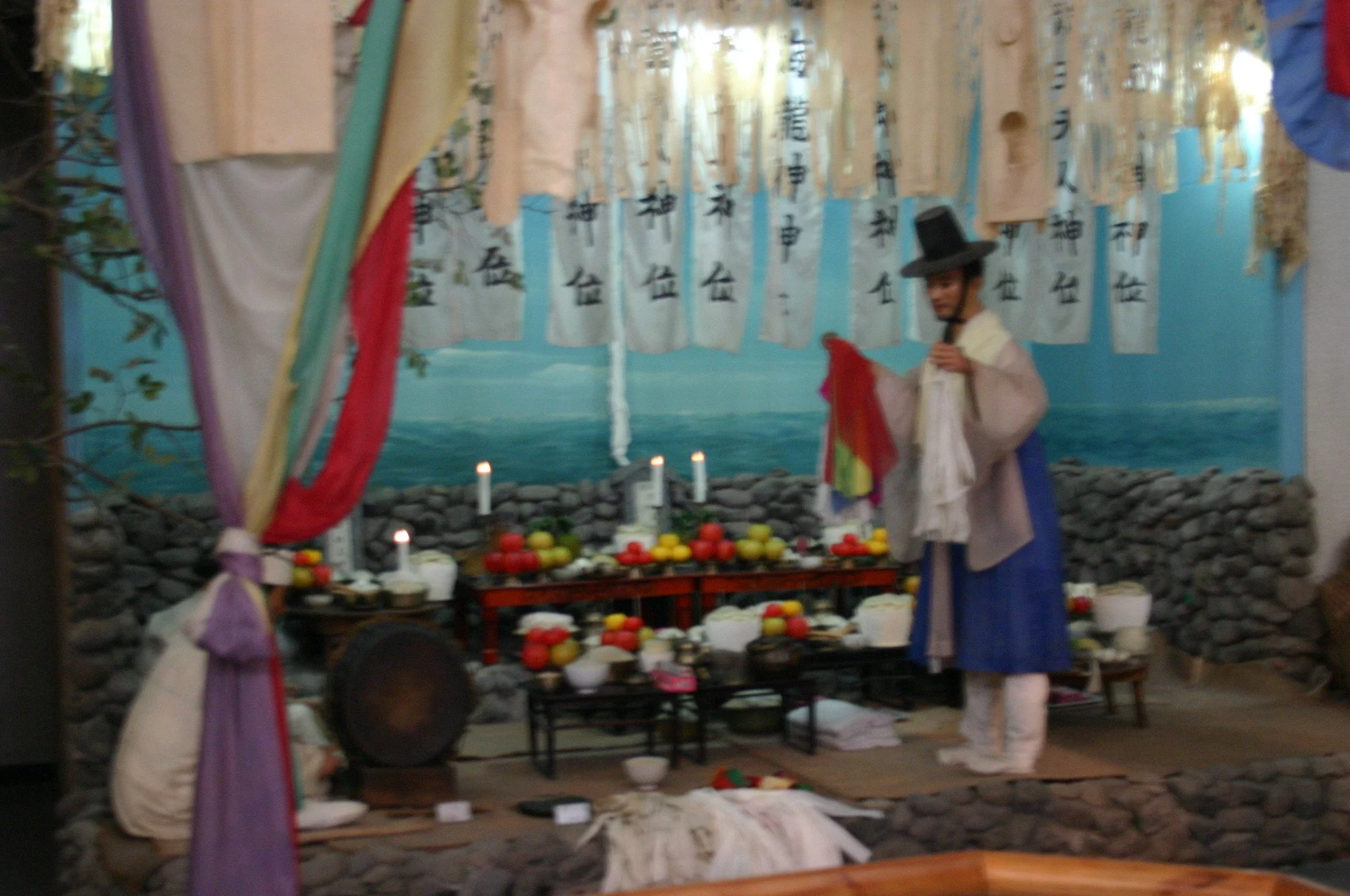 Museum display of a Korean shaman performing a gut ritual, with an altar and ceremonial costumes