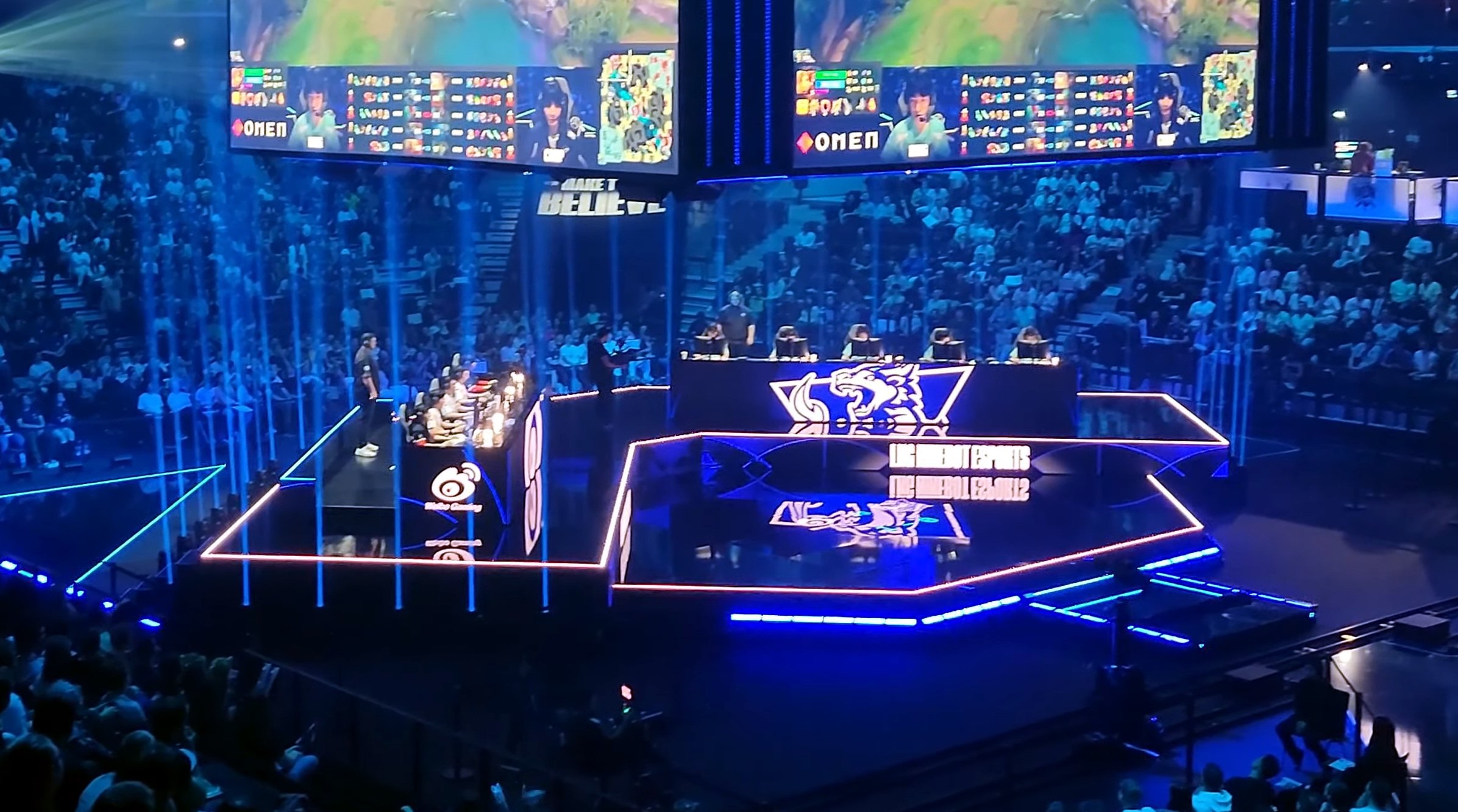 Wide view of the 2024 League of Legends World Championship quarterfinal stage, with players at their desks under large screens and a packed arena around them.