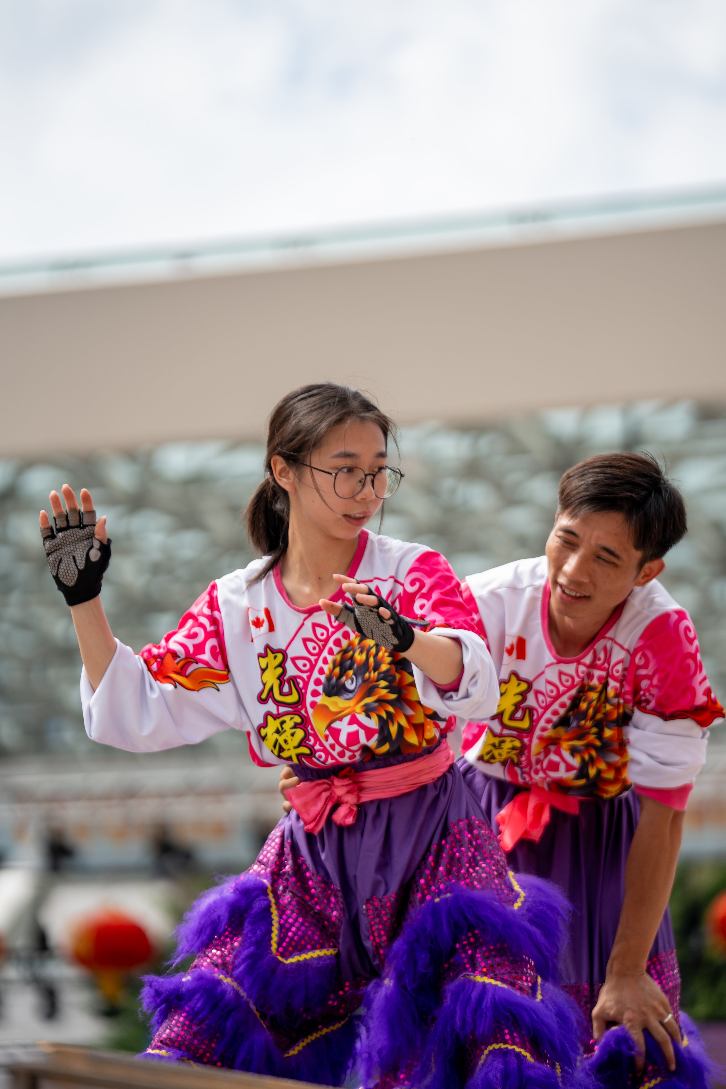Two performers in colorful traditional costumes, featuring animal designs and vibrant patterns, engaged in a dance routine outdoors.