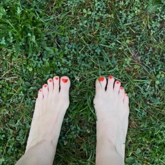 Füße mit orangen Nagellack im grünen Gras.