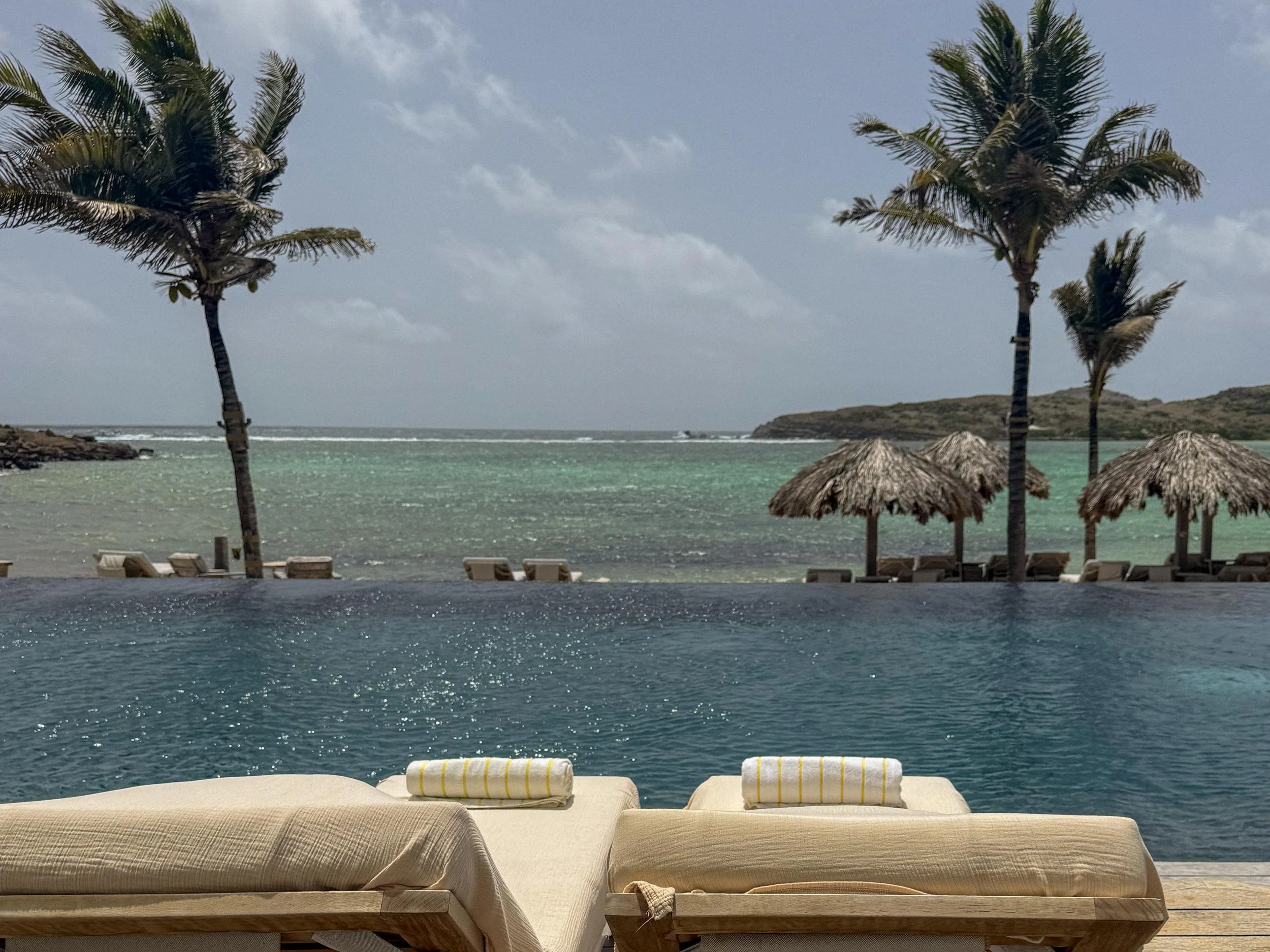 Infinity pool overlooking the calm turquoise lagoon and palapas at Rosewood Le Guanahani.