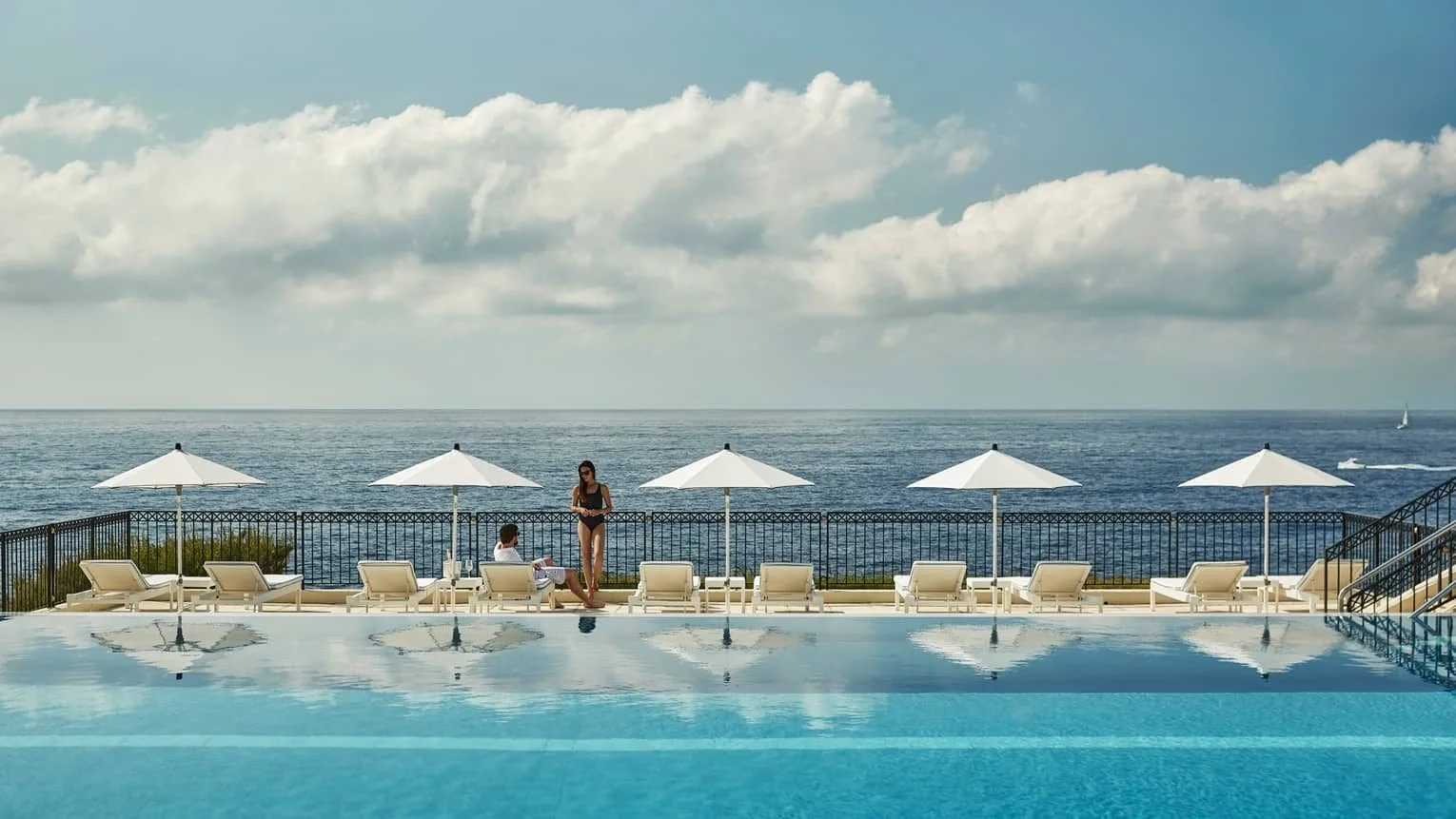 The Club Dauphin infinity pool at Grand-Hôtel du Cap-Ferrat overlooking the Mediterranean horizon with white loungers and umbrellas.