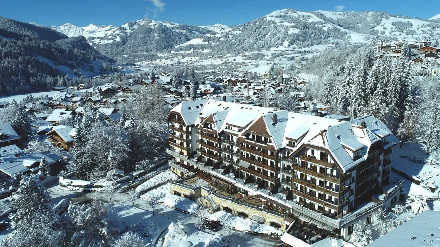 Aerial view of The Park Gstaad, A Four Seasons Hotel, above the snow-covered village of Gstaad in the Swiss Alps