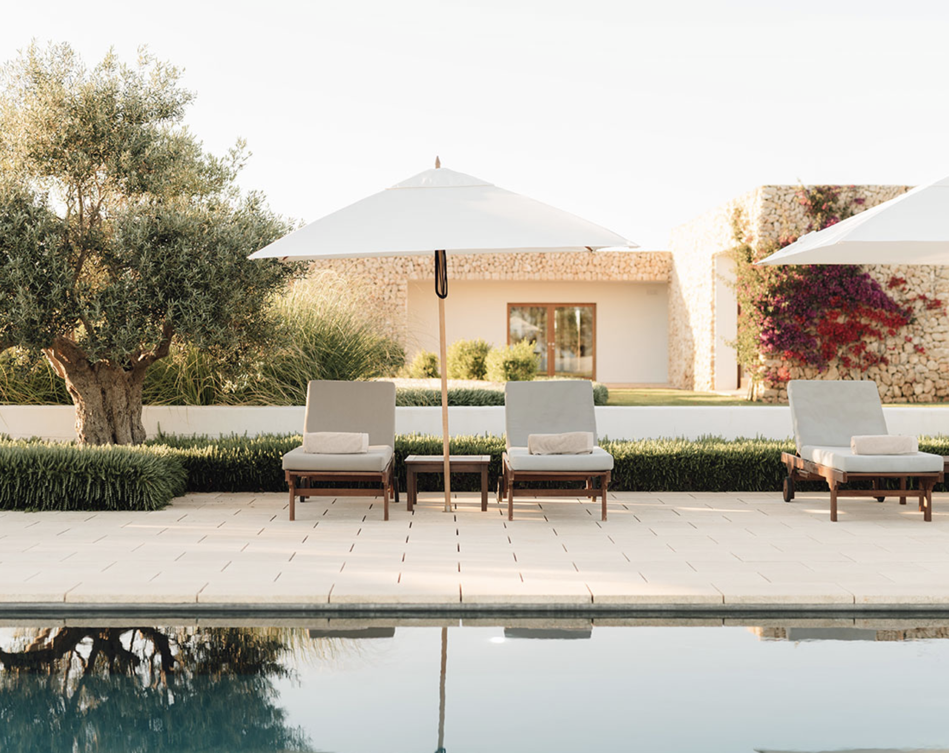 Sun loungers and parasols beside an outdoor swimming pool framed by olive trees and stone walls at Hotel Torralbenc, Menorca.