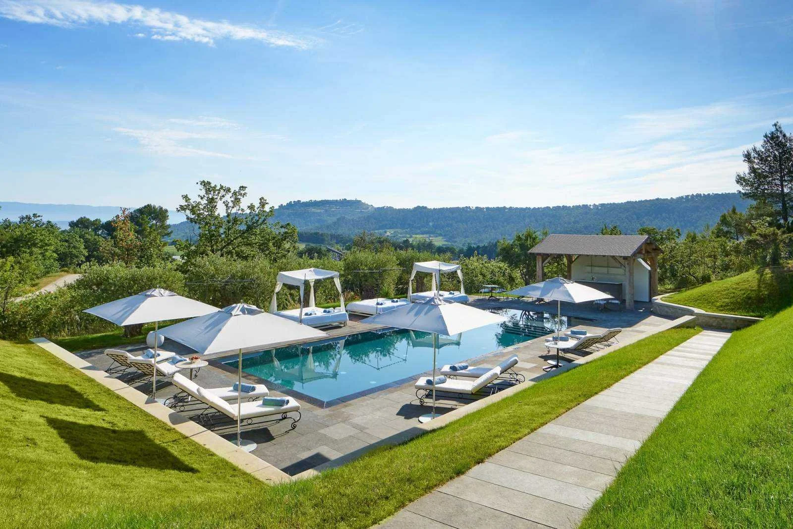 Infinity pool at Villa La Coste in Provence, white loungers and parasols on a hilltop terrace with vineyards and hills in the distance.