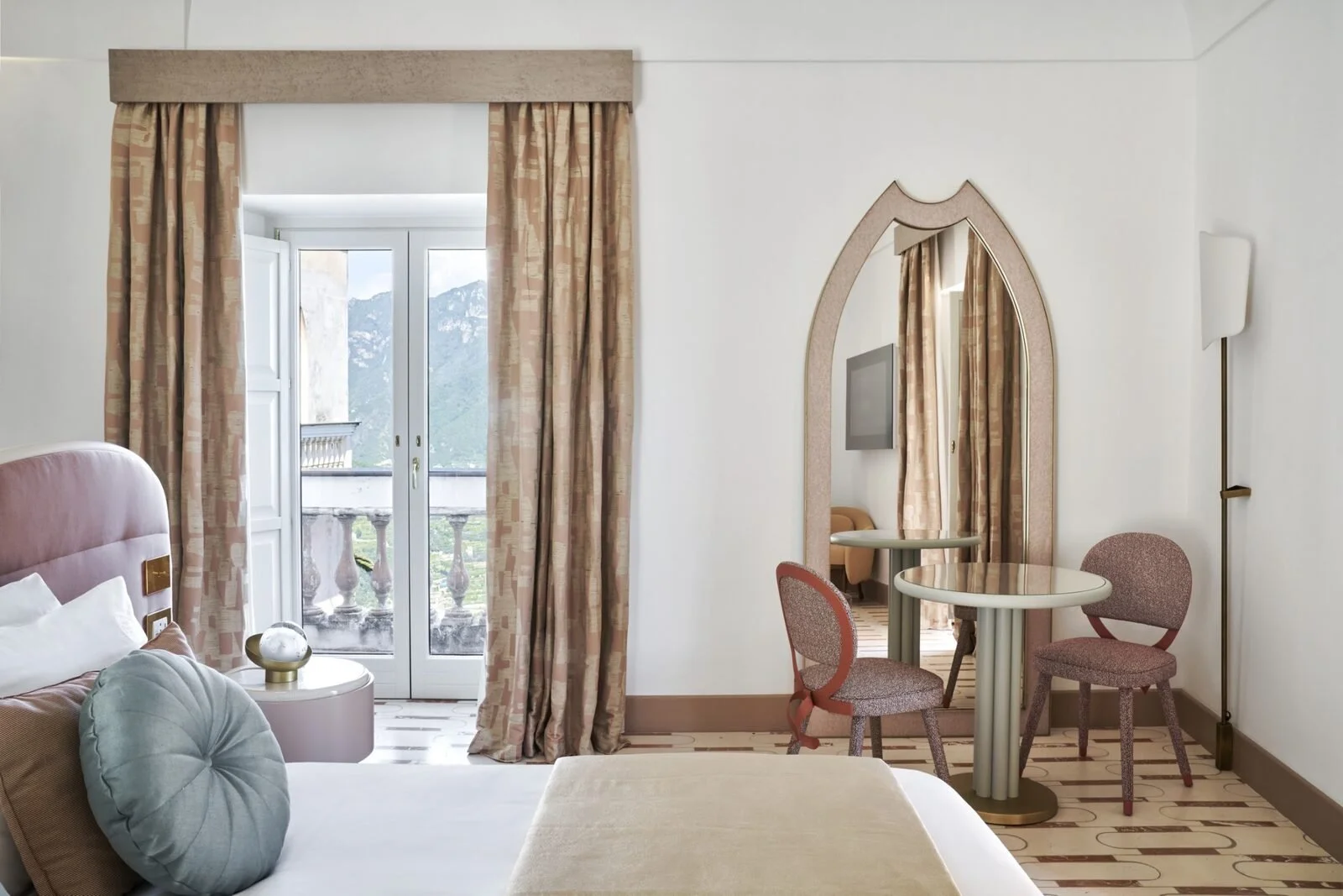 Room at Palazzo Avino in Ravello in blush and pink tones with an arched mirror and doors open to a balcony