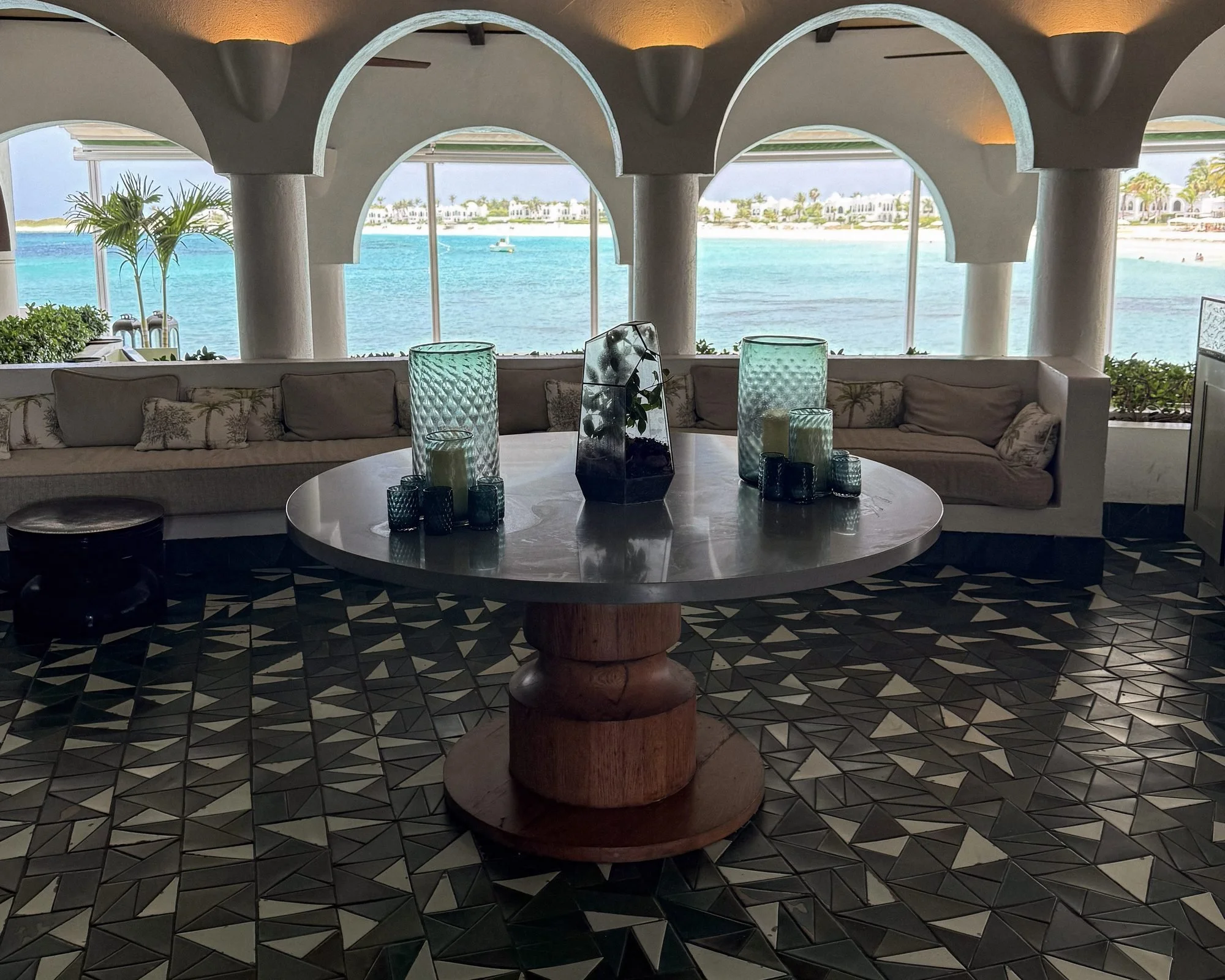 Open-air lounge with white arches and geometric tile floors framing a turquoise ocean view