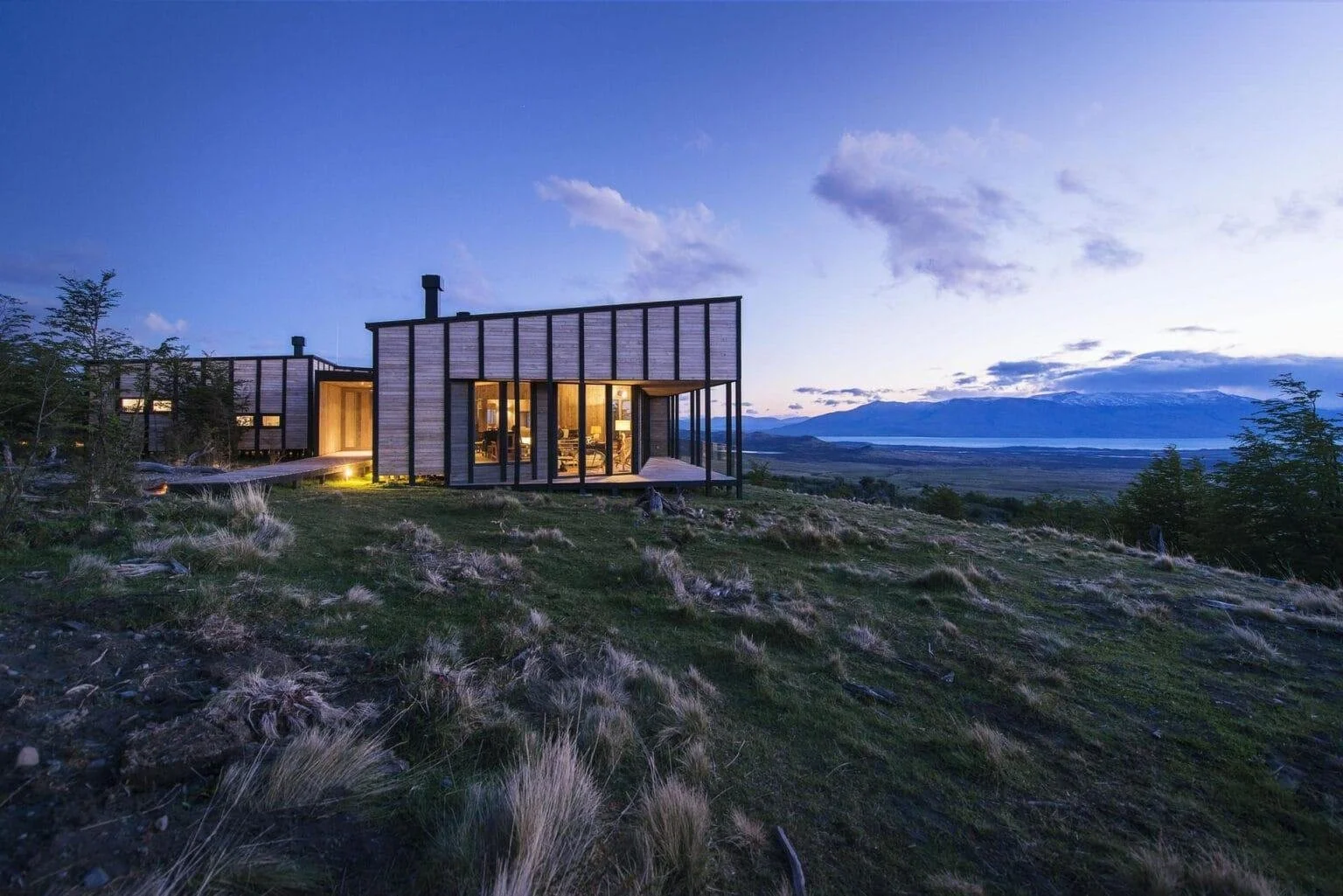 Standalone timber villa at Awasi Patagonia at dusk, set on a hillside above Lake Sarmiento