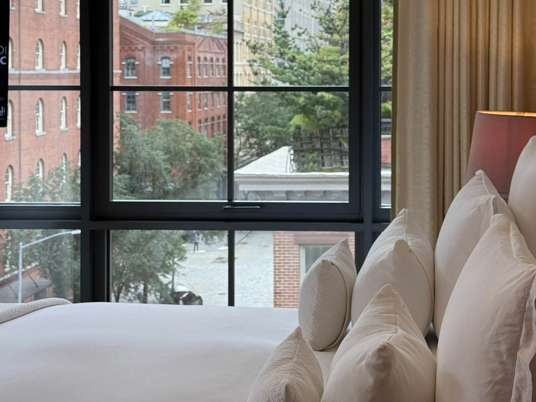 Fouquet's New York Deluxe Room bed with plush white linens facing black grid windows and Tribeca brick views