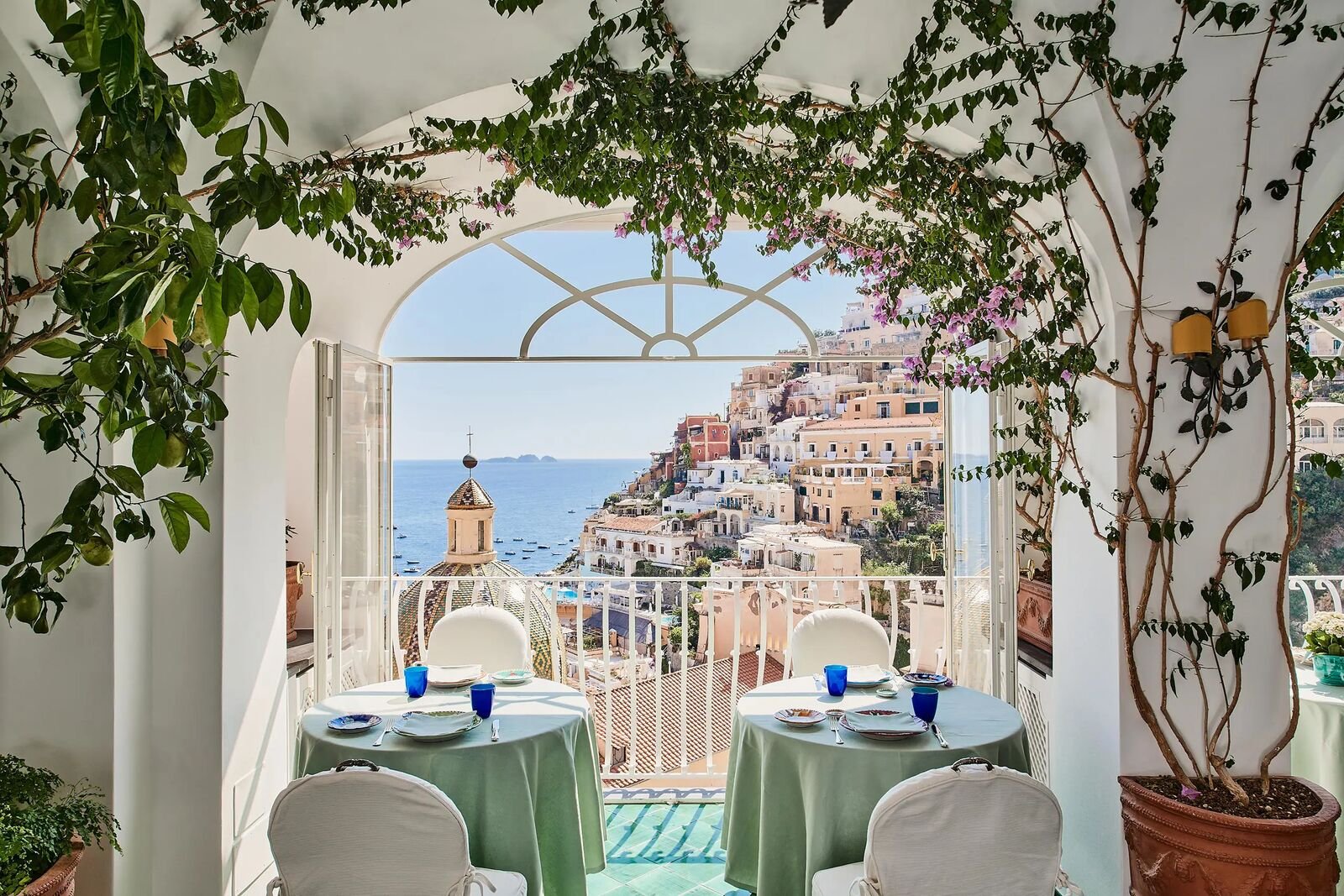 Mesas de comedor dispuestas bajo un arco de buganvillas en Le Sirenuse, con vistas a Positano y al mar