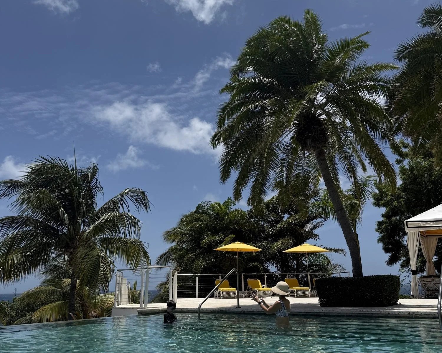 Kate Van Dell and son playing catch in Malliouhana infinity pool with blue sky and palm trees
