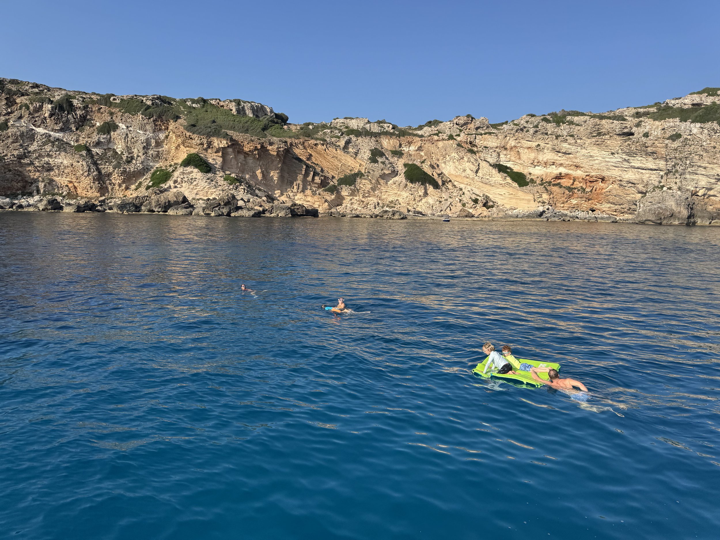 Swimmers and a float in a deep blue cove below limestone cliffs, Menorca, Spain