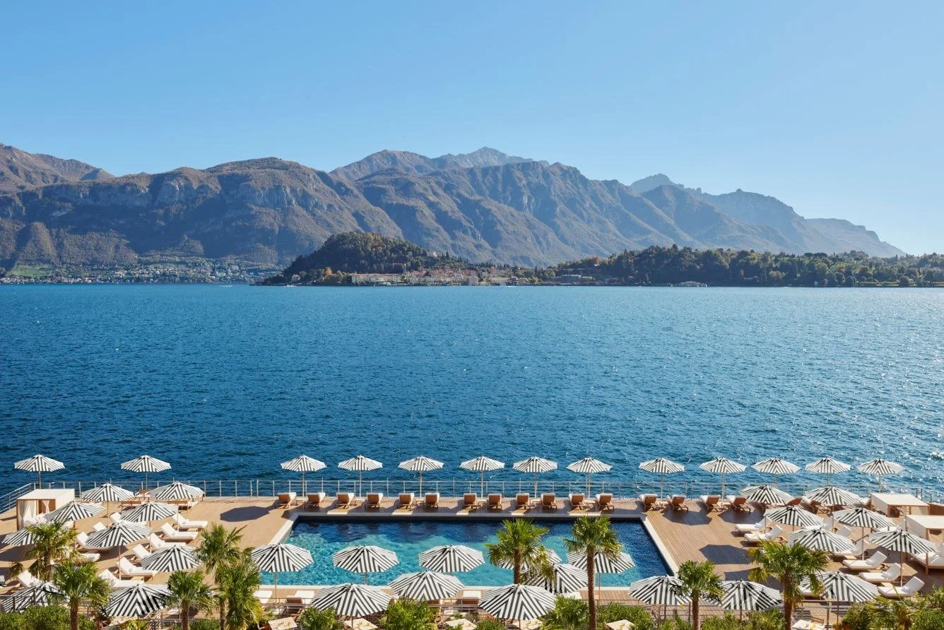 Floating pool and striped umbrellas at The Lake Como EDITION in Cadenabbia, looking across the lake to Bellagio