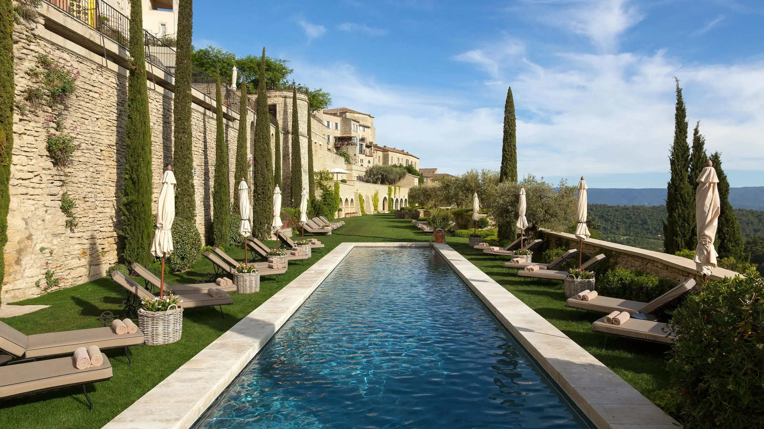 Lap pool lined with cypresses and sun loungers below the village at Airelles Gordes, La Bastide
