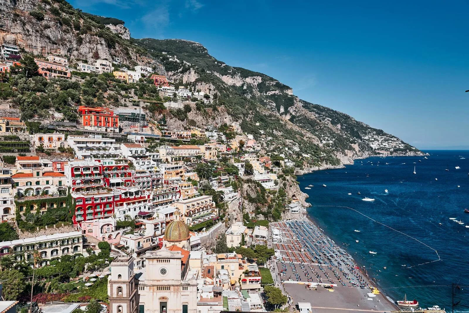 View across Positano from above showing the red Le Sirenuse building, terraced houses and the beach on the Amalfi Coast