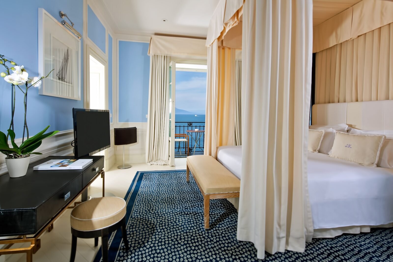 Sea view room at J.K. Place Capri with a canopy bed, blue walls and doors open to a balcony over the bay