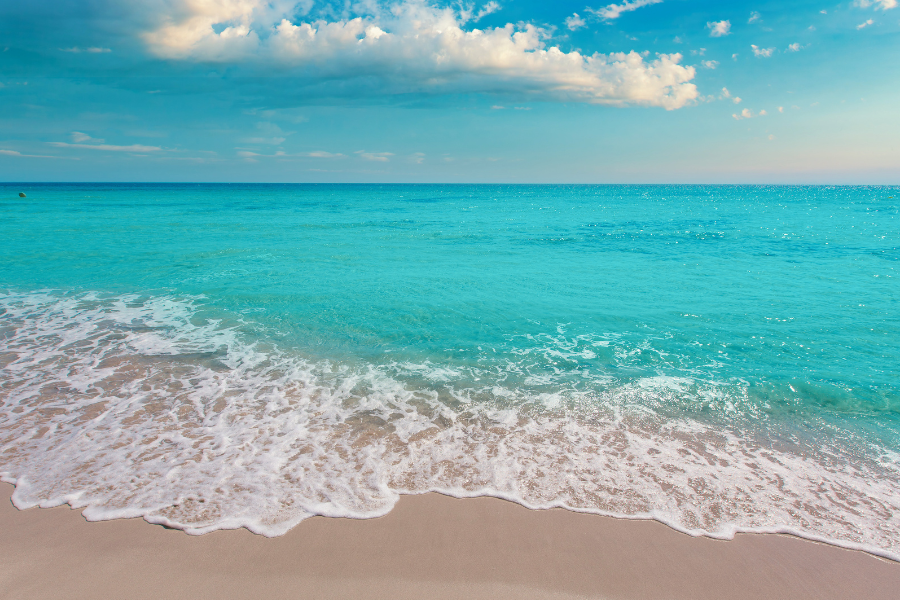 一片宁静的海滩，碧绿清澈的海水，轻柔的波浪，以及半晴半阴的天空。