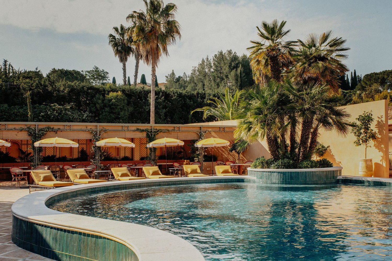 Curved pool with yellow parasols and palms at Mas Candille in Mougins