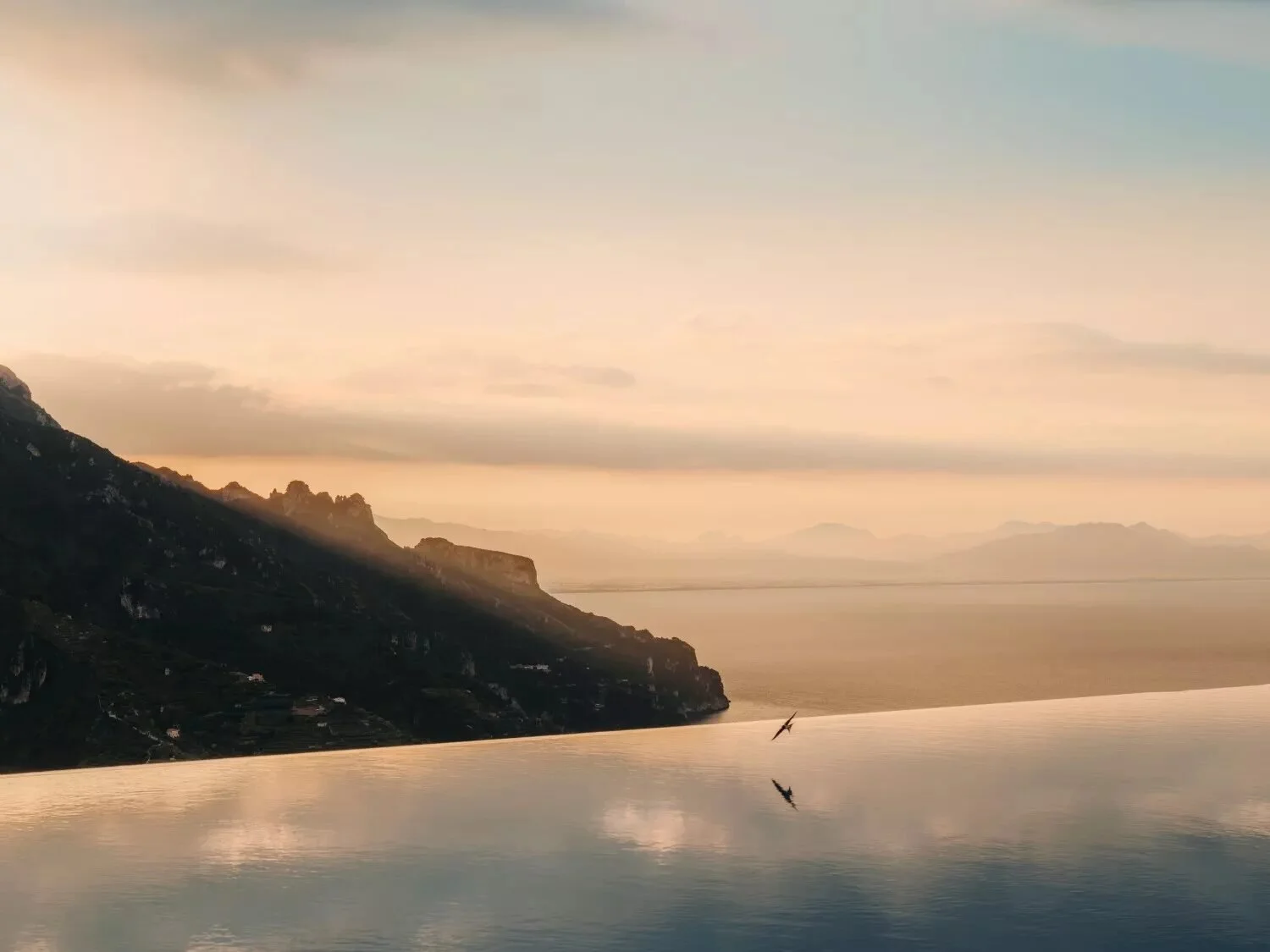 Piscina infinita climatizada del Caruso, un hotel Belmond, en Ravello, con la logia de piedra y la torre del reloj reflejadas a la primera luz del día