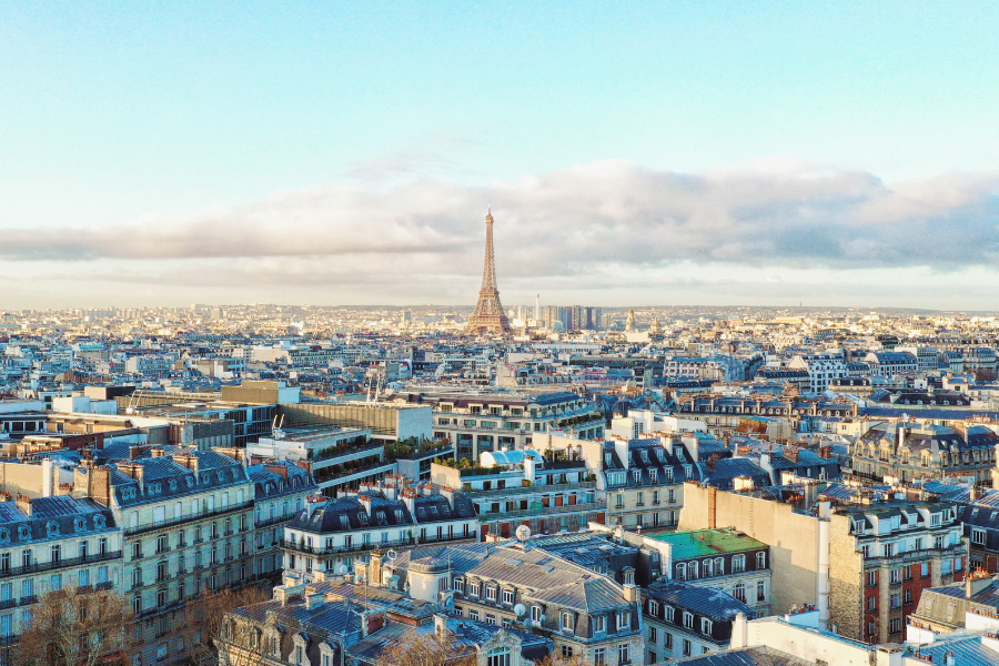 巴黎鸟瞰图：远方矗立着埃菲尔铁塔，在多云的天空下，经典的巴黎建筑群环绕其间。