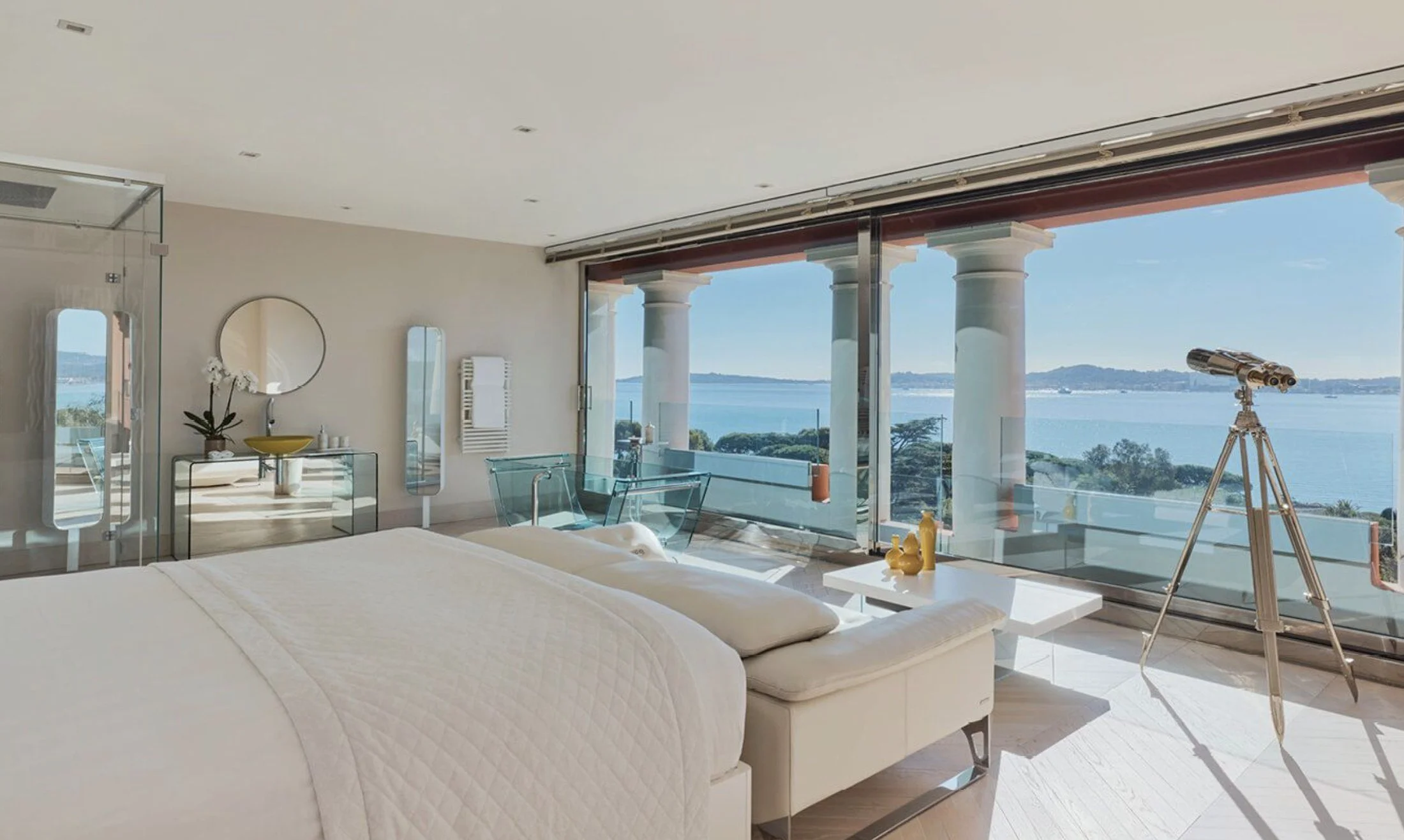 Bedroom with floor to ceiling glass opening onto a colonnaded terrace and the Gulf of Saint-Tropez at COMO Le Beauvallon