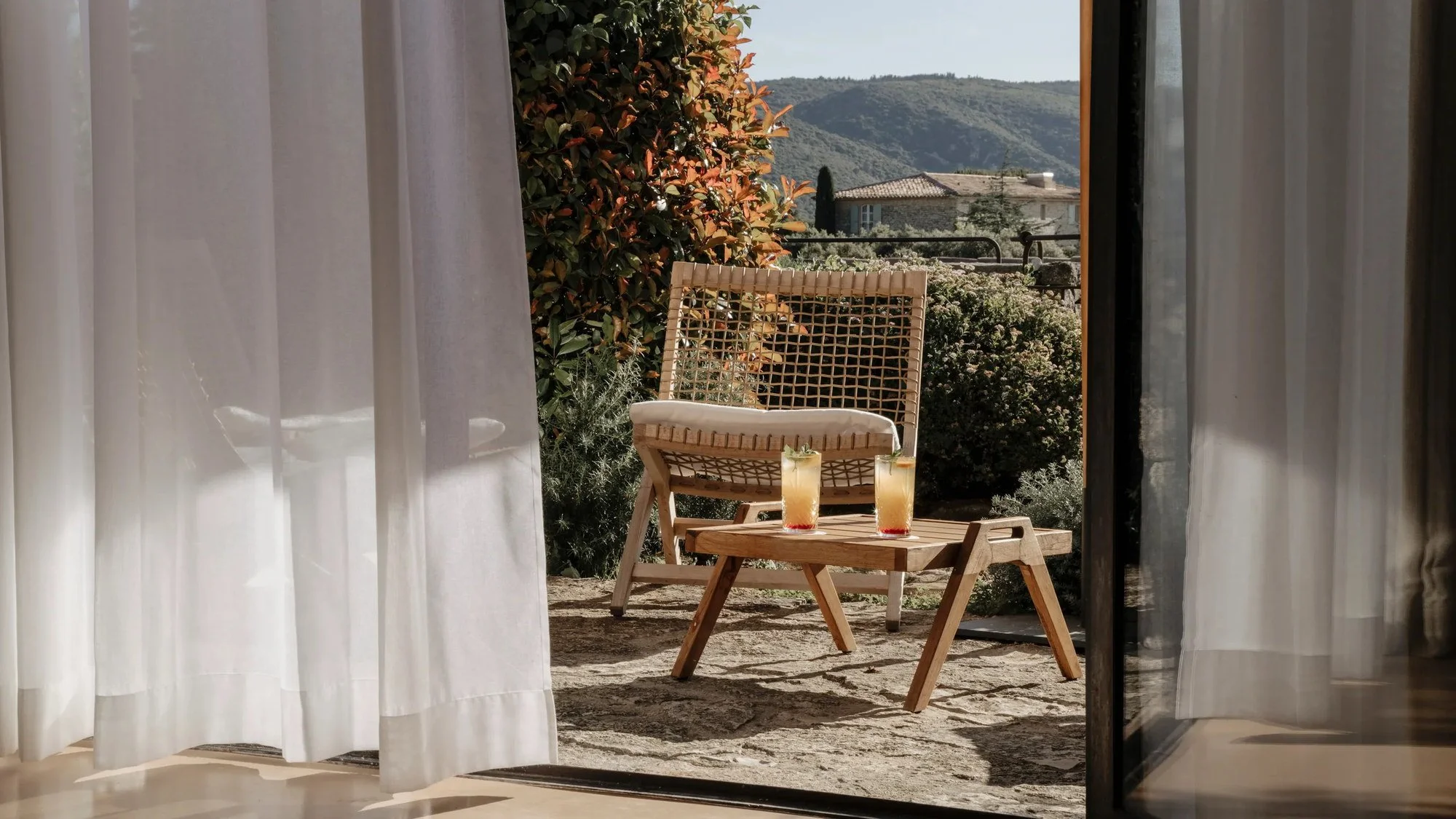 View from a Capelongue guest room through open doors to a private terrace and the Luberon hills.